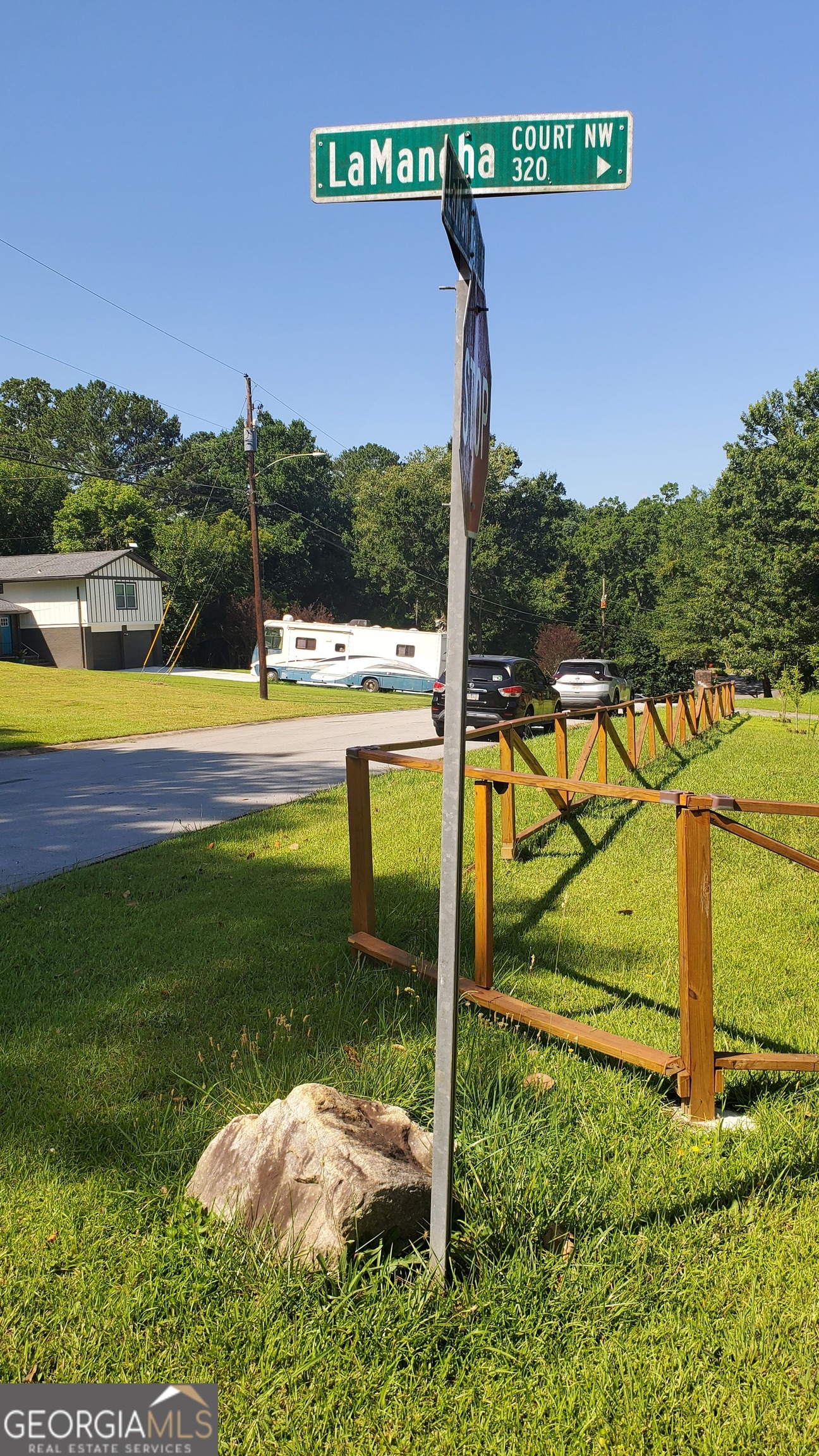 Vacant grassy lot beside LaMancha Court NW, marked by a street sign and wooden fencing.