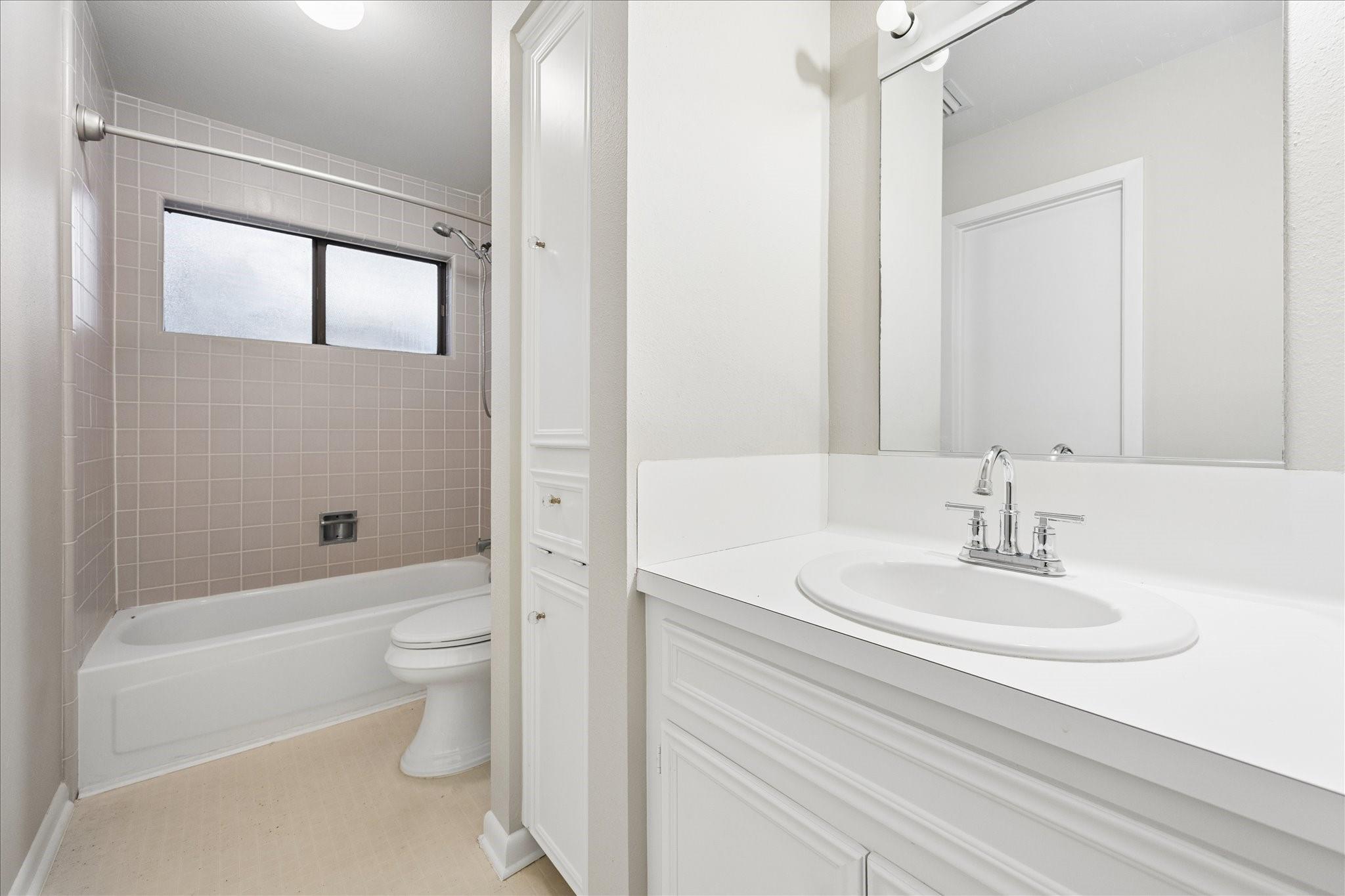 Bathroom with a tiled tub and shower beside a white vanity with an oval sink.