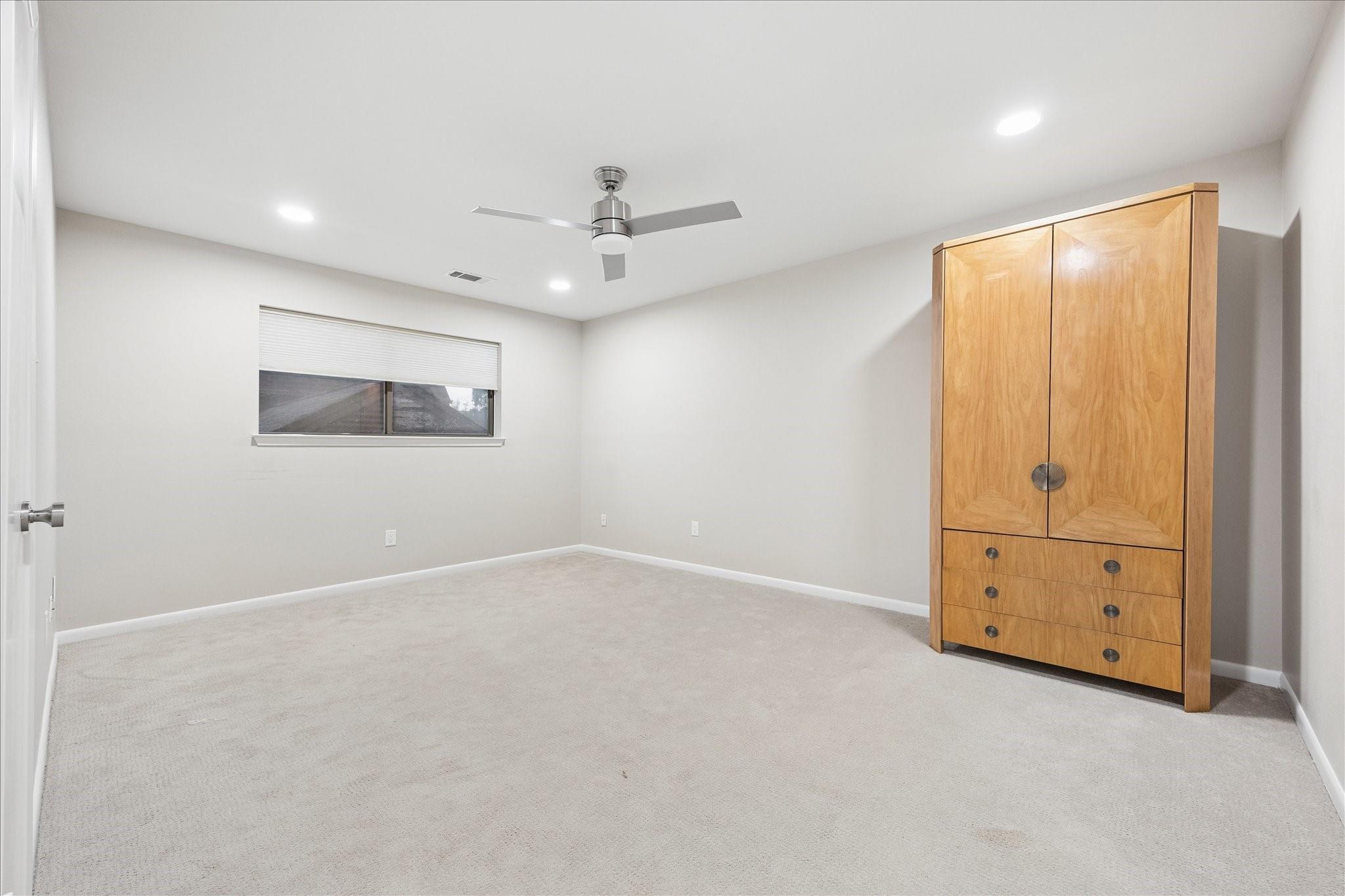 Carpeted bedroom with a ceiling fan, partially covered window, and large wooden wardrobe.