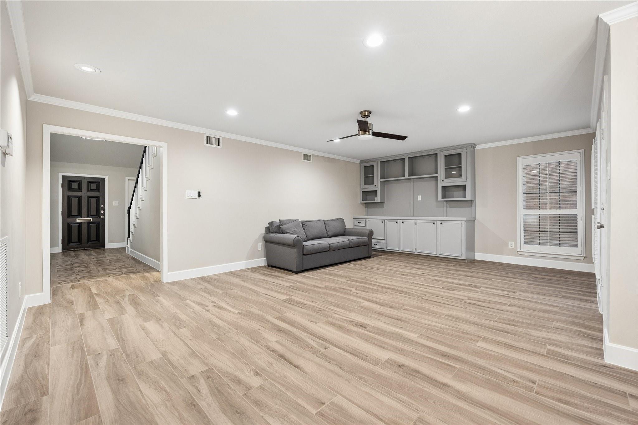 Living room with wood-look floors, gray sofa, built-in cabinetry, and an open view to the entryway.