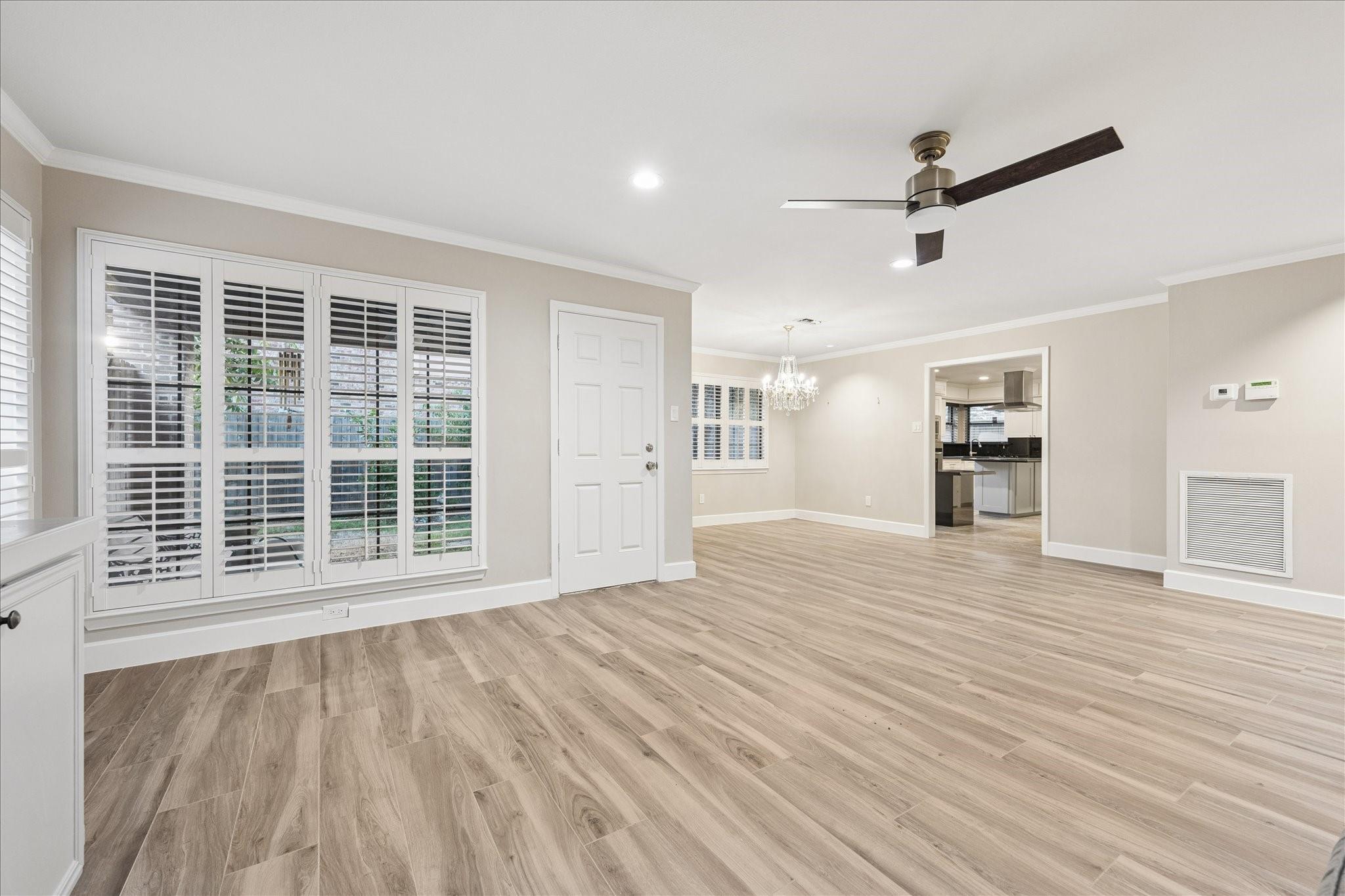 Vacant living room with wood-look flooring, plantation shutters, and an open view into the kitchen.