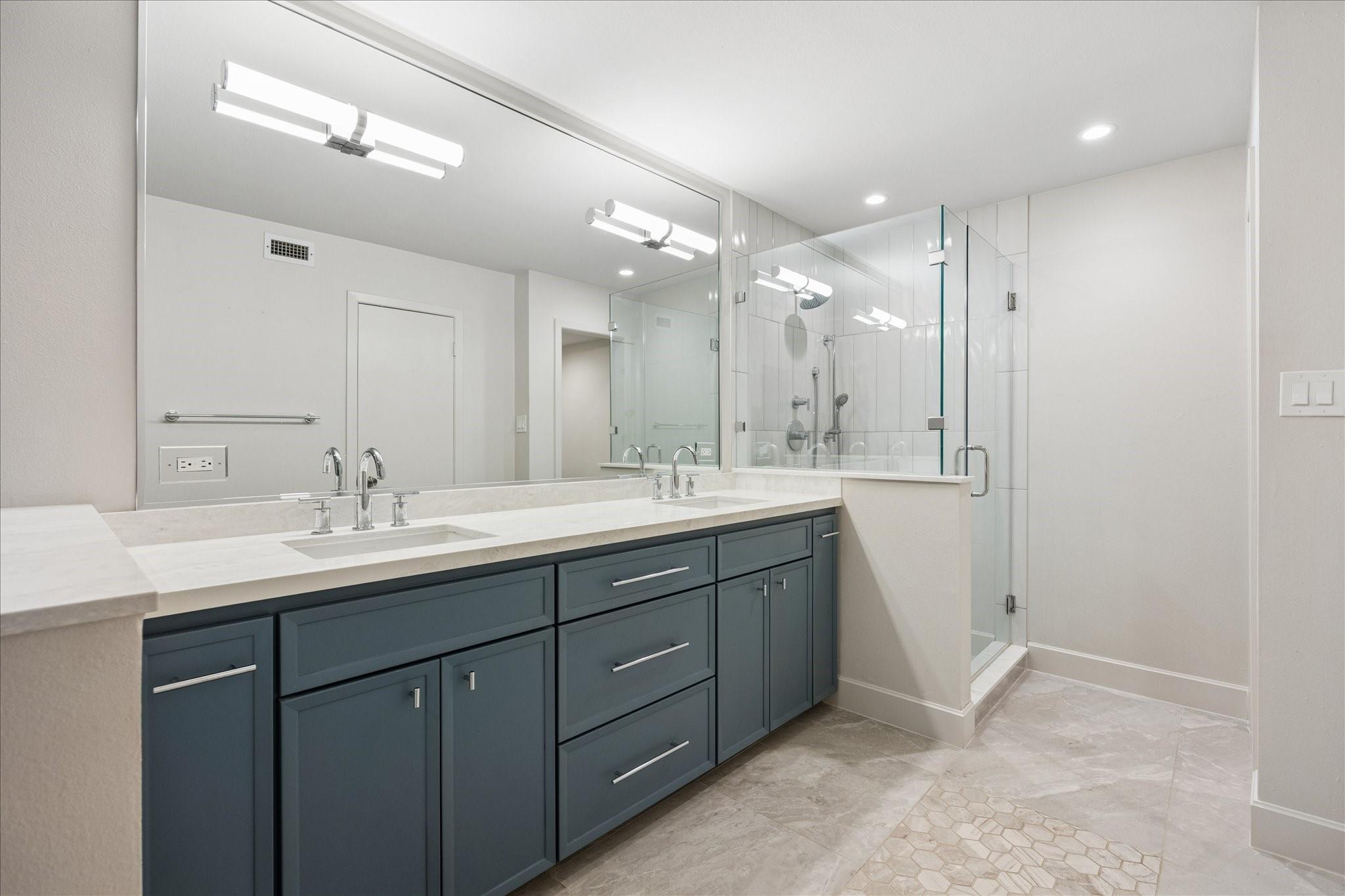 Bathroom with a double vanity, blue-gray cabinets, and a glass-enclosed tiled shower.