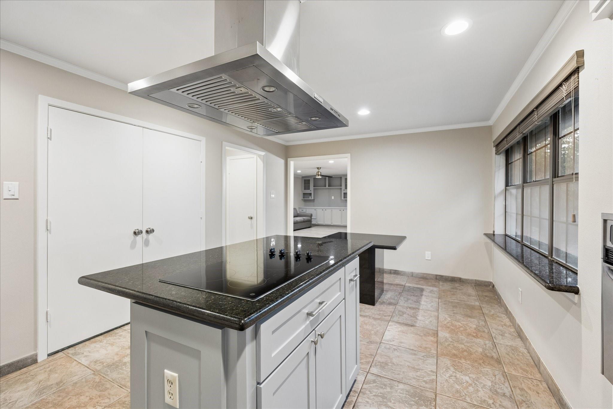 Kitchen with a white island, dark countertop and cooktop beneath a stainless steel range hood.