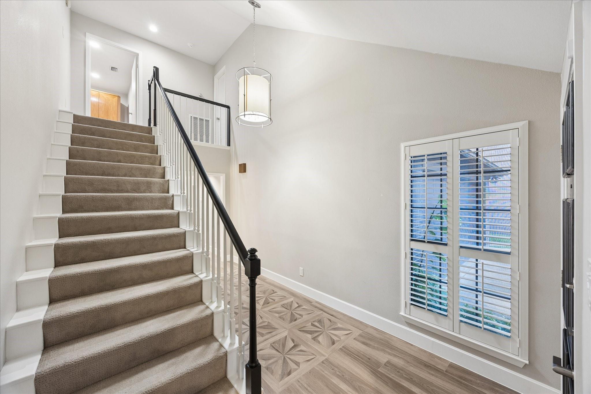 Foyer with a carpeted staircase, geometric wood flooring, and a large shuttered window.