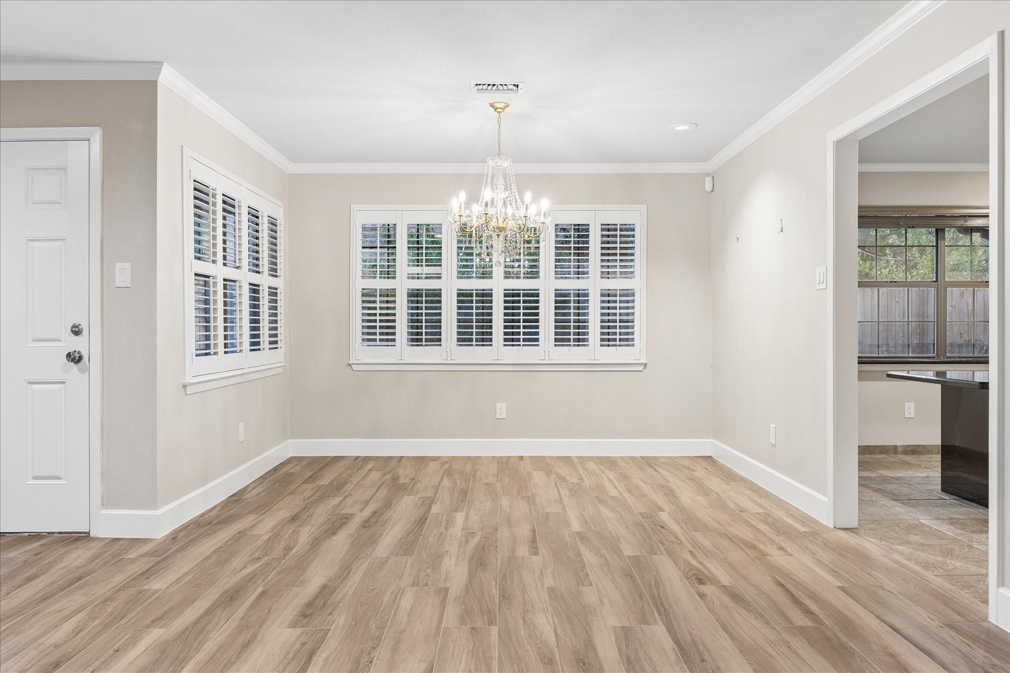 Empty dining room with plantation shutters, a crystal chandelier, and light wood-look flooring.