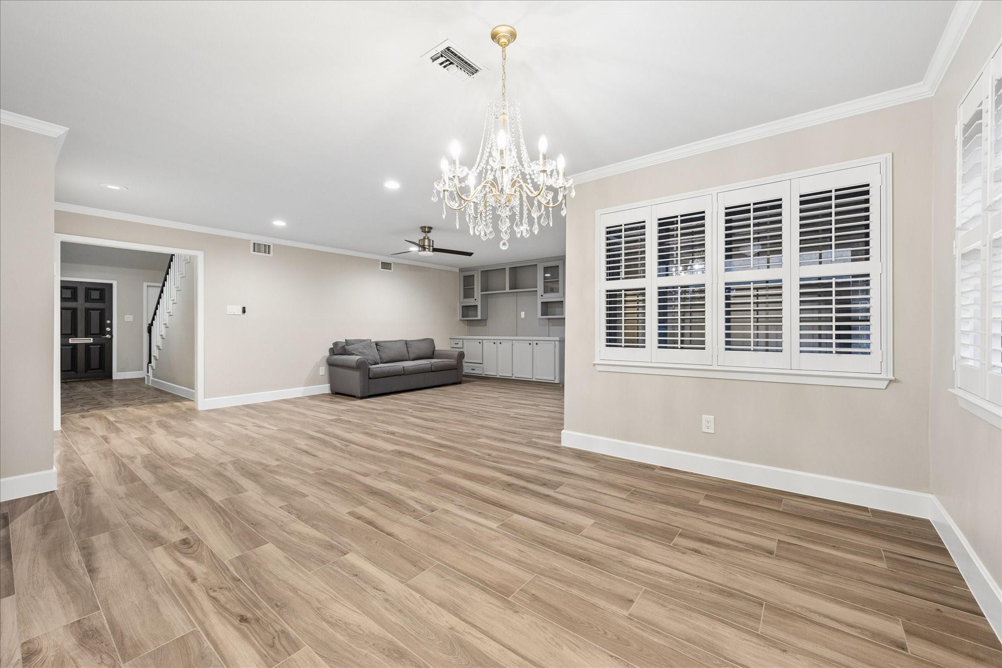 Living room with wood-look tile floors, gray sofa, built-in cabinets, chandelier, and plantation shutters.