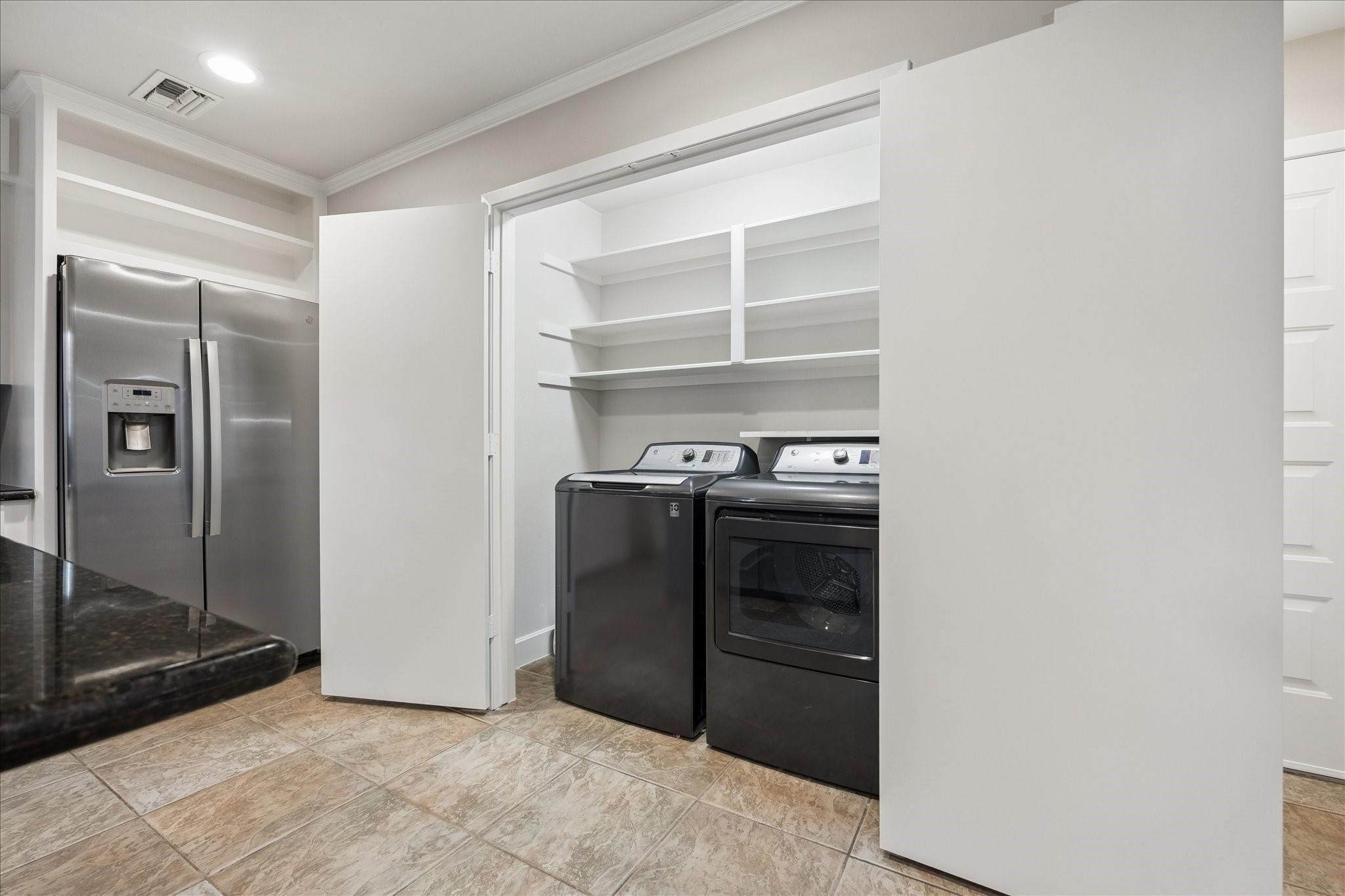 Laundry area with washer and dryer behind open white doors beside a stainless steel refrigerator.