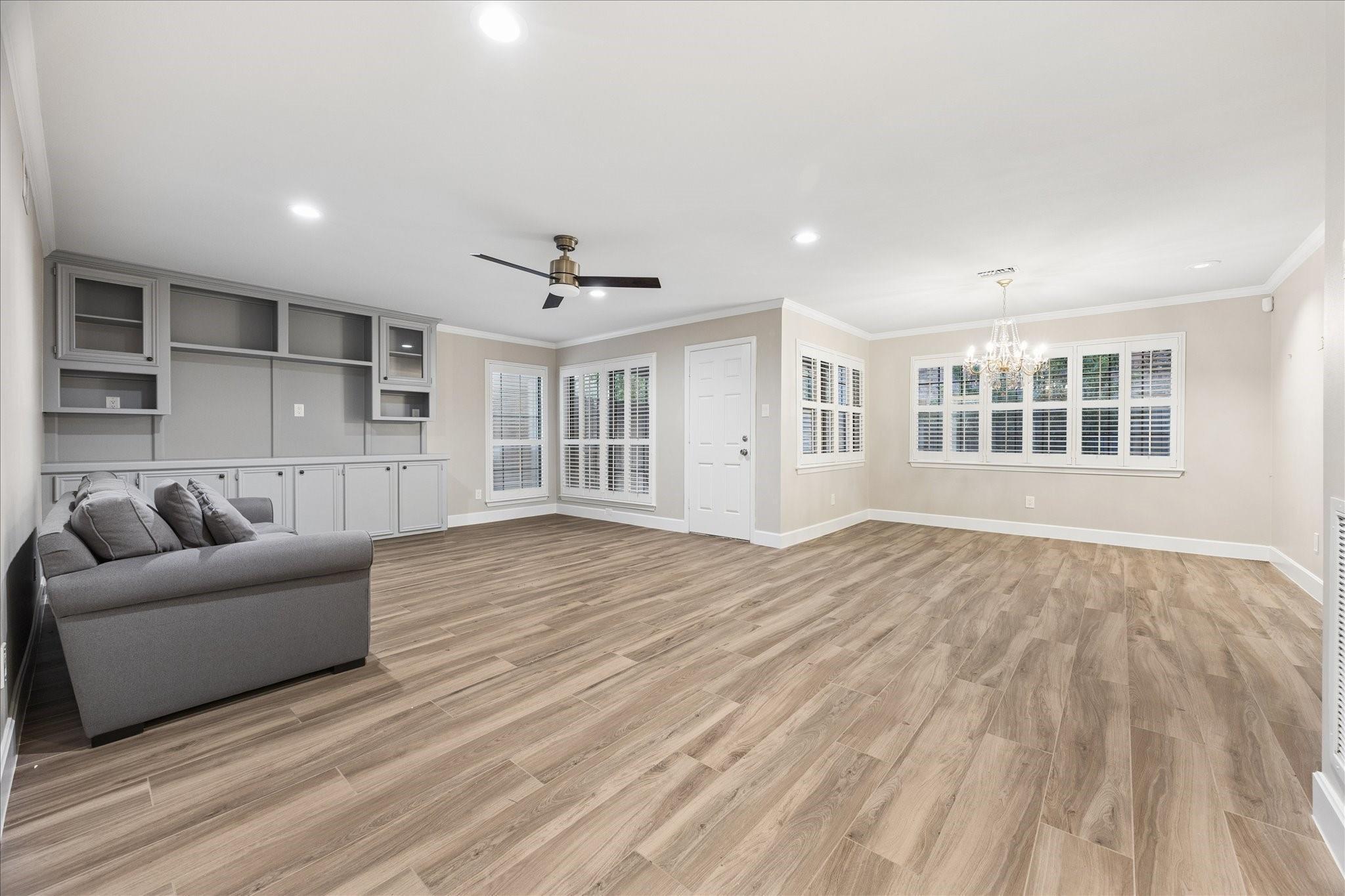 Living room with gray built-ins, a sofa, wood-look floors, shuttered windows, and a chandelier.