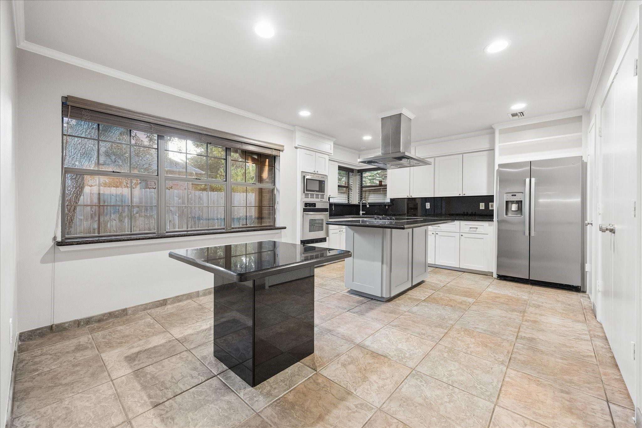 Kitchen with white cabinets, black countertops, stainless appliances, a central island, and large windows.