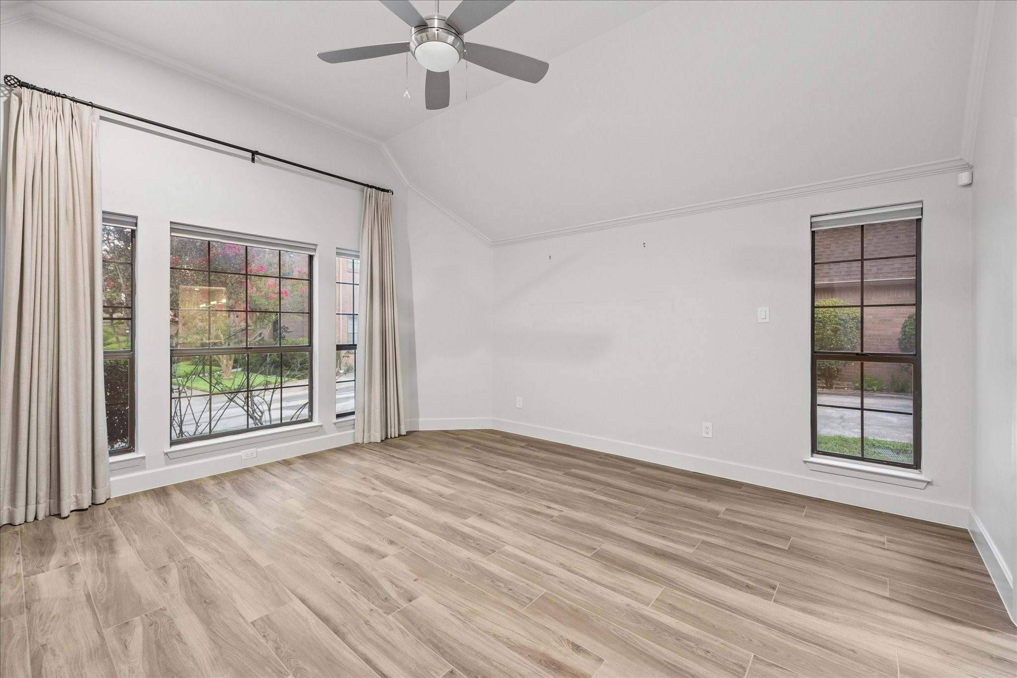 Empty bedroom with a high sloped ceiling, ceiling fan, large curtained windows, and wood-look tile flooring.