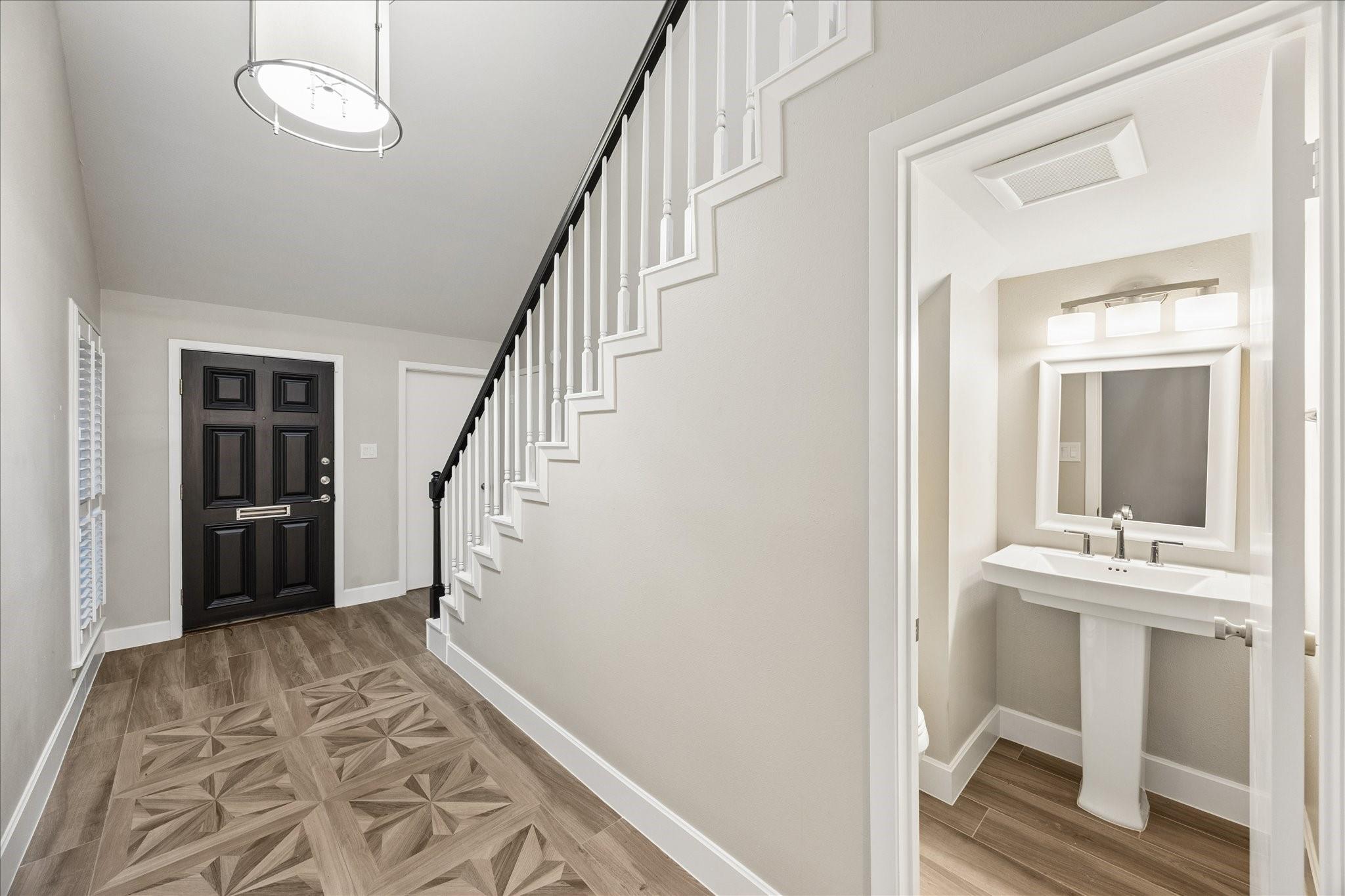 Entry foyer with patterned tile, a staircase, and a powder room with pedestal sink.