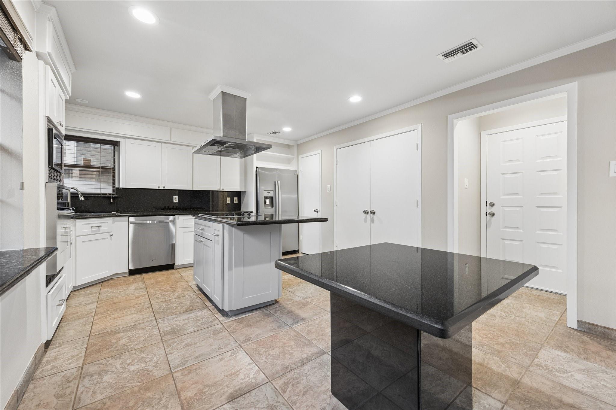 Kitchen with a black granite island, white cabinets, stainless steel appliances, and tan tile floors.