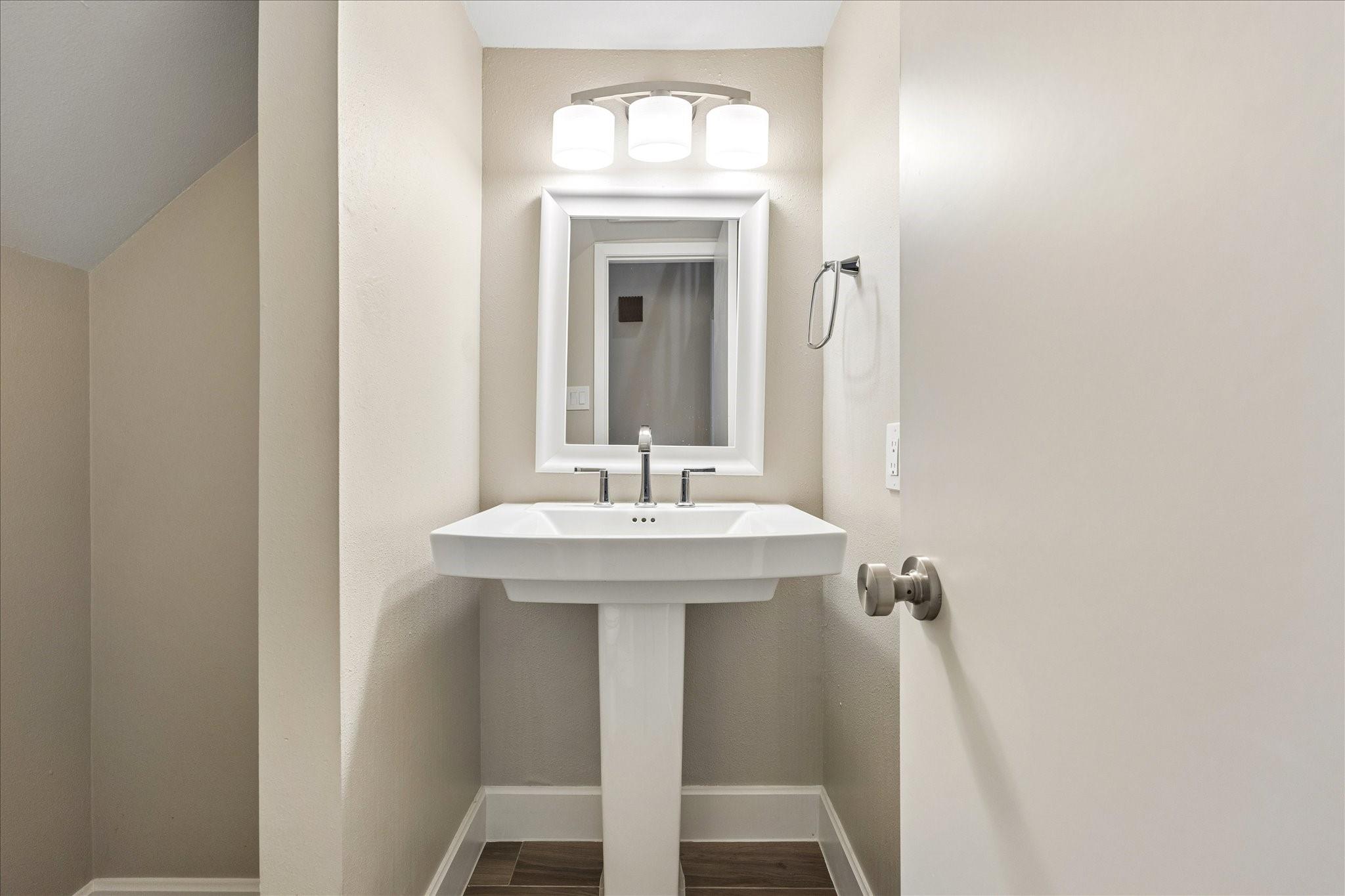 Bathroom vanity with a white pedestal sink, framed mirror, and three-light fixture.