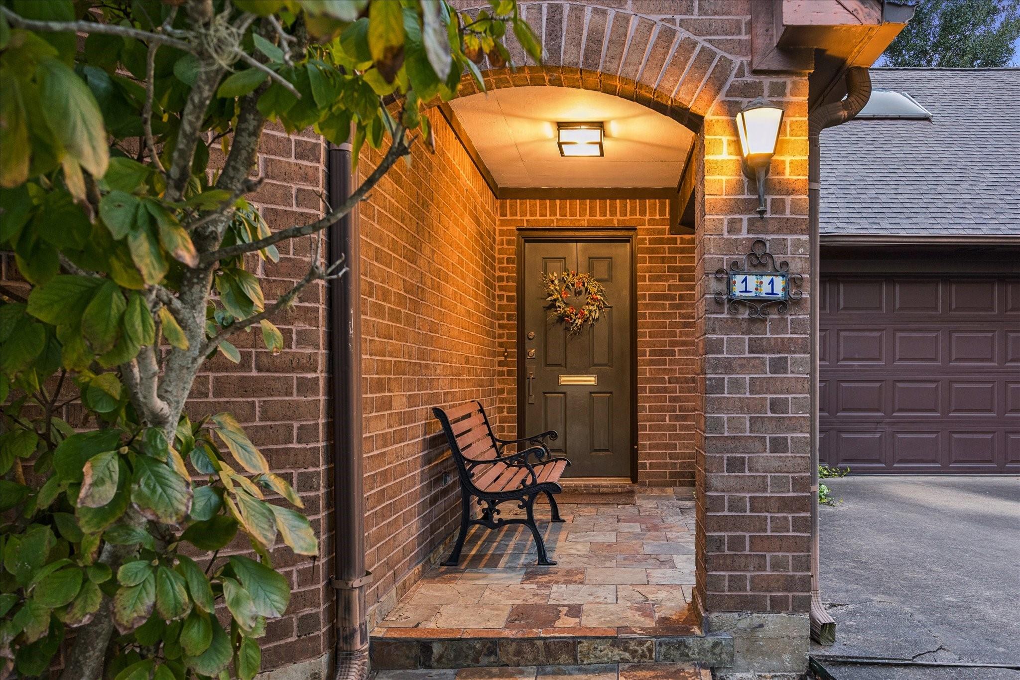 Brick home entrance with a covered porch, wreath-adorned door, stone paving, and attached garage.