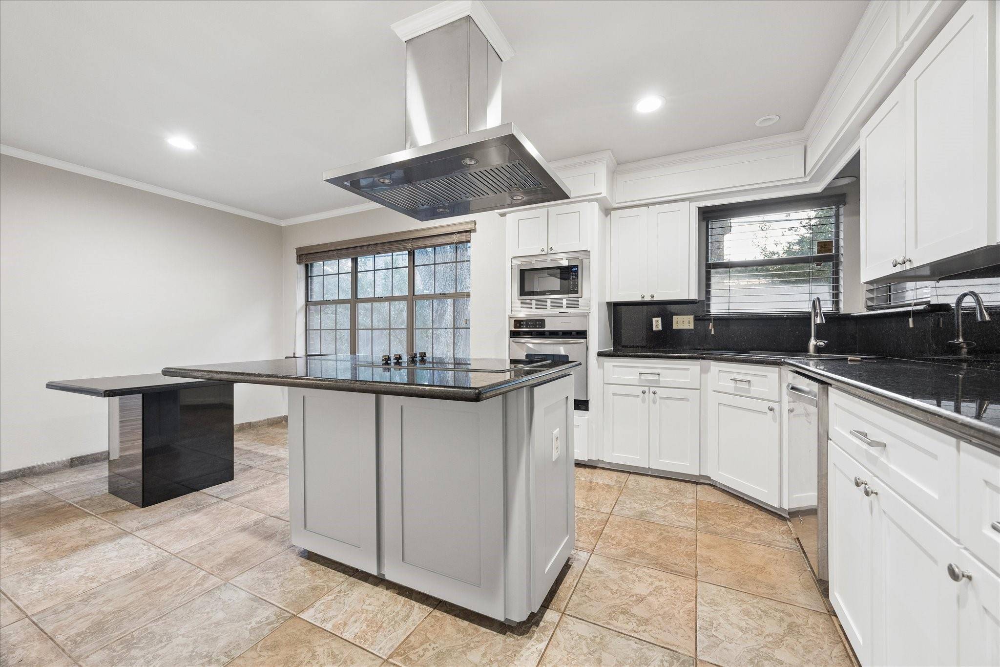 Kitchen with a large island, black countertops, white cabinetry, and built-in appliances.