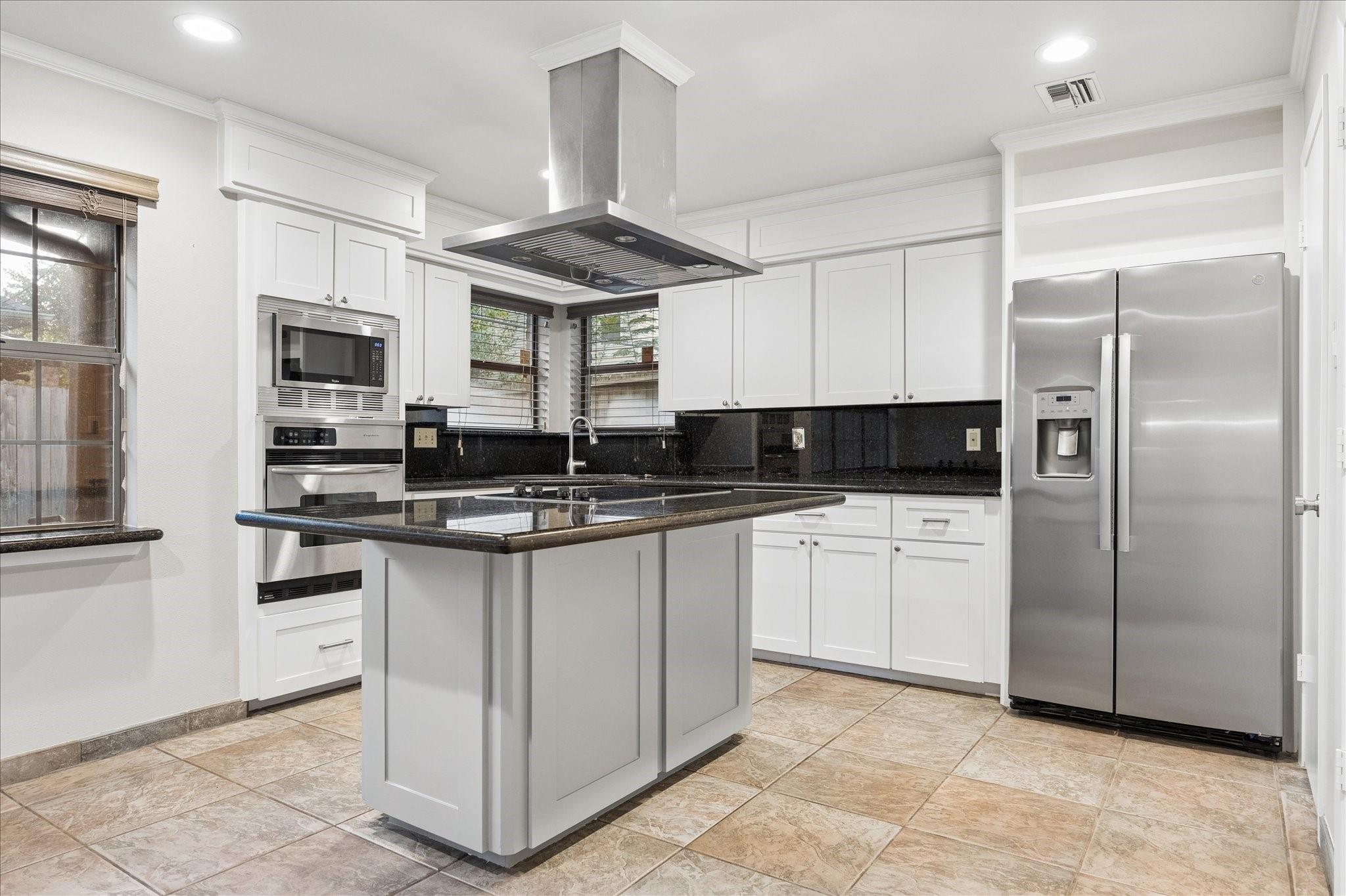 Kitchen with a large cooktop island, white cabinets, black countertops, and stainless-steel appliances.
