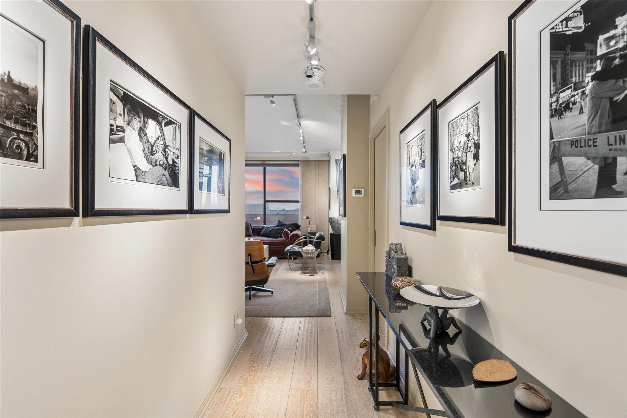 Furnished hallway lined with framed photographs and a console table, opening into a living room with a large window.