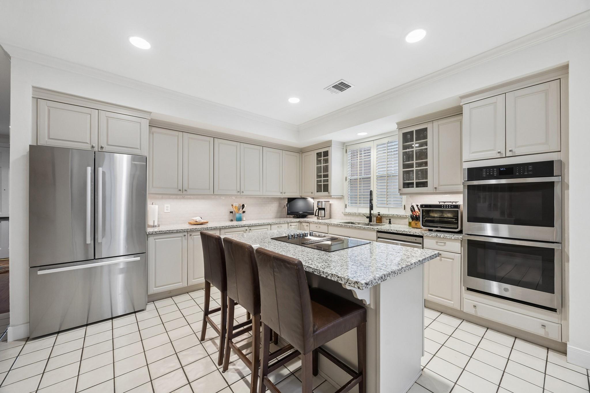 Kitchen with a granite island, bar seating, stainless steel refrigerator, and built-in double ovens.