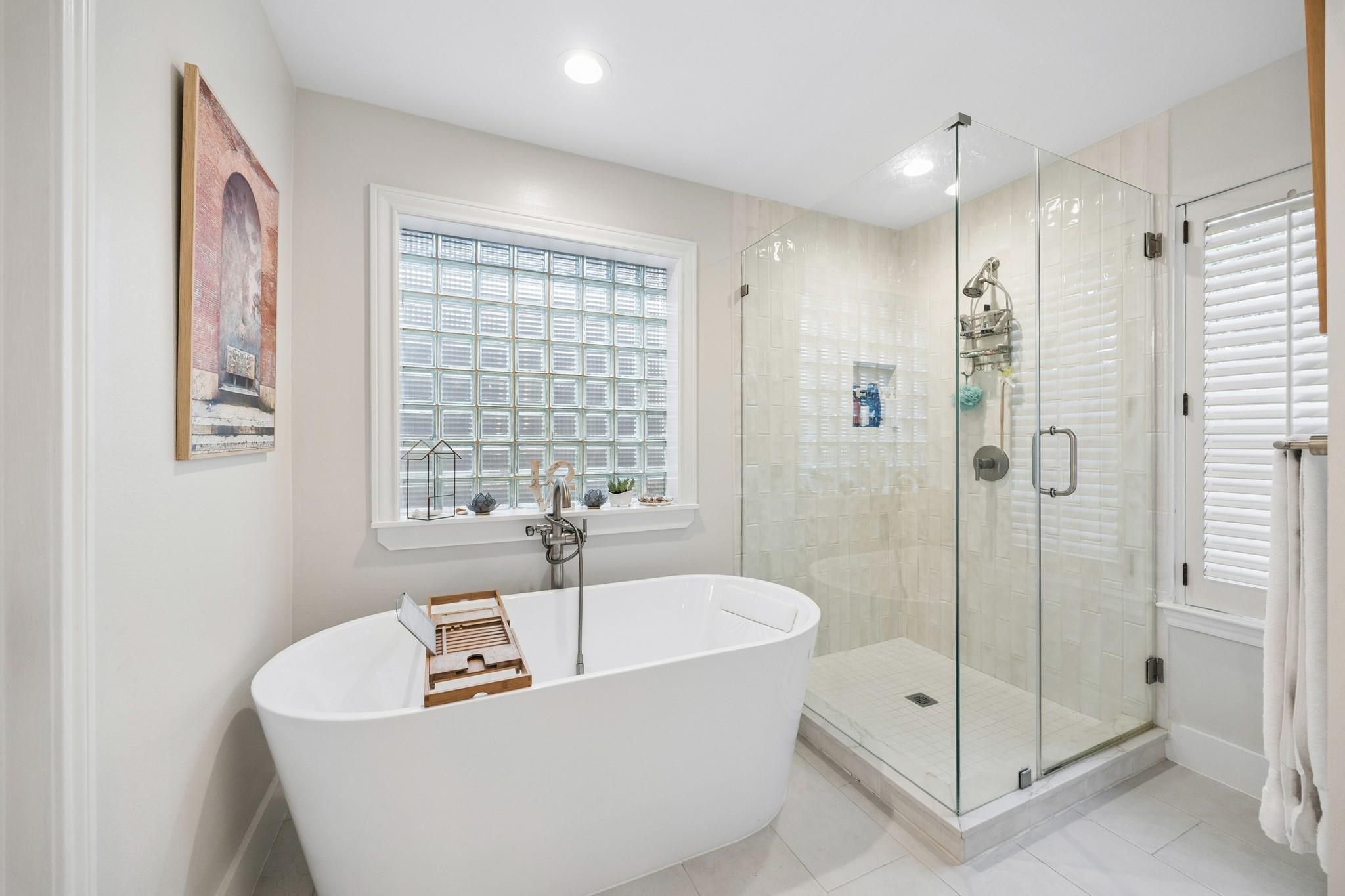 Bright bathroom with a freestanding soaking tub, glass-enclosed shower, and glass-block window.