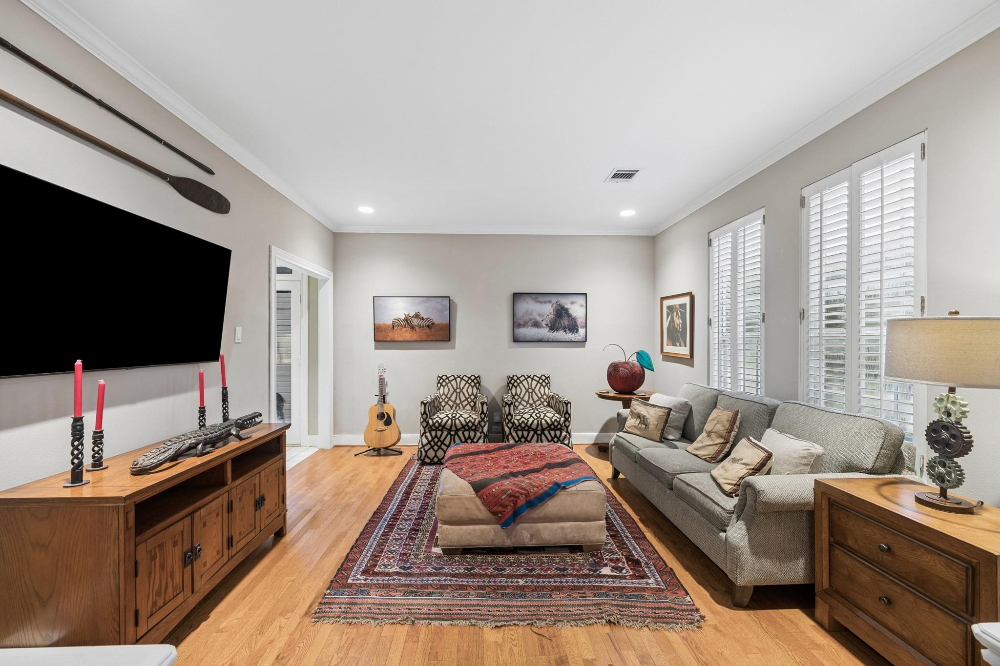 Living room with hardwood floors, a wall-mounted television, patterned chairs, and tall shuttered windows.