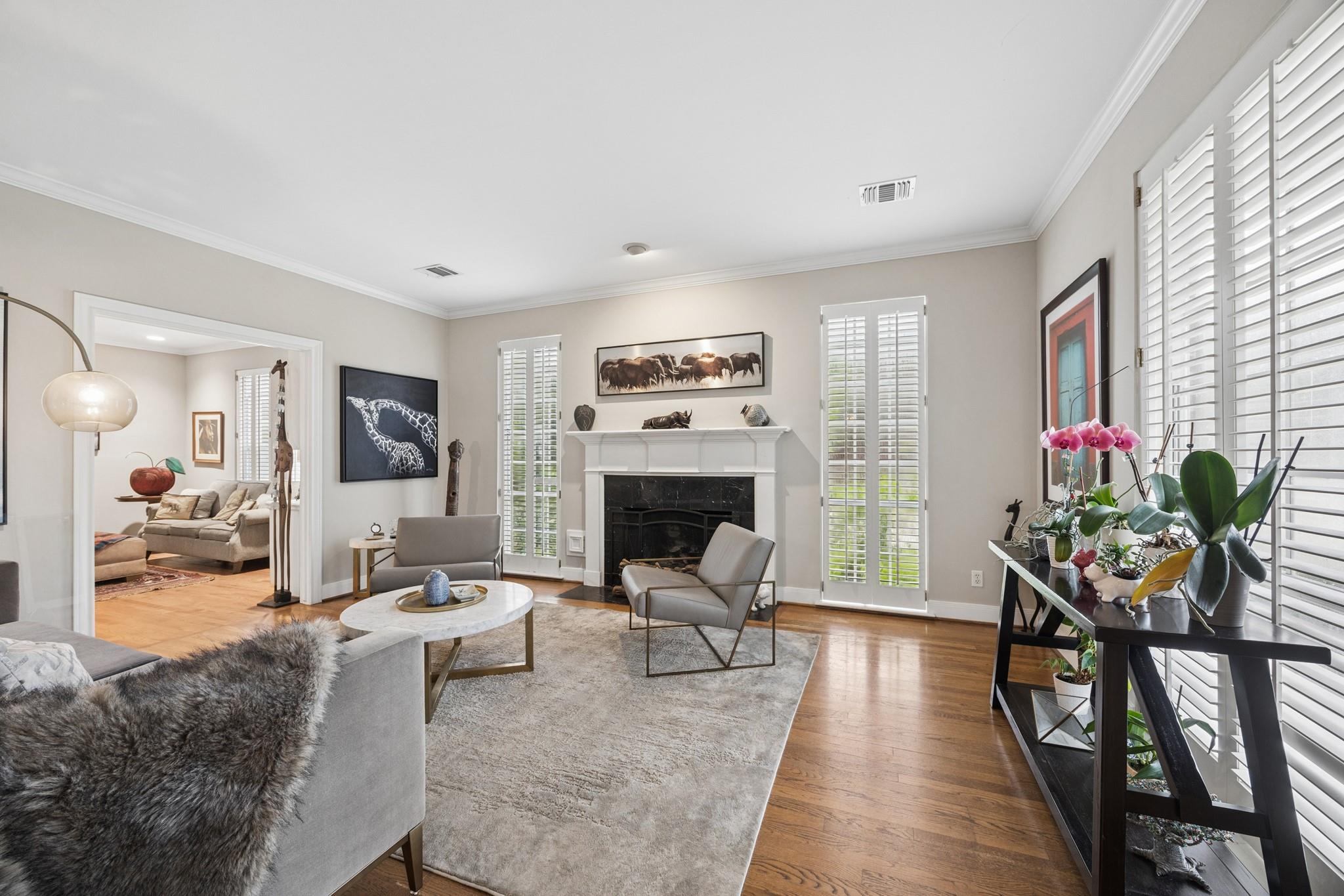 Living room with a white fireplace, gray seating, hardwood floors, and tall shuttered windows.