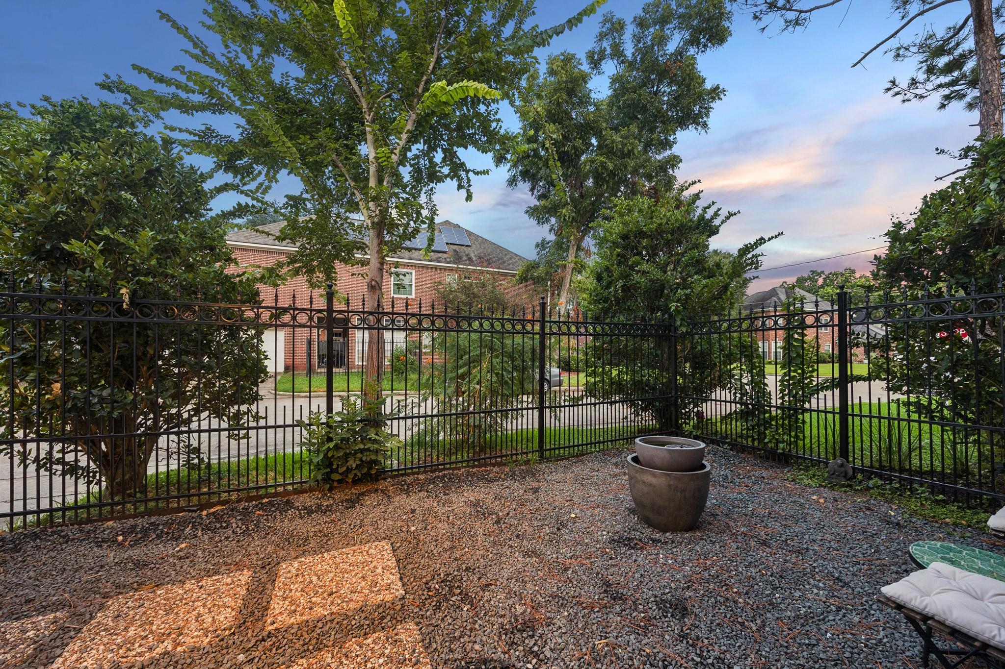 Gravel patio with a wrought-iron fence, potted fire bowl, and cushioned outdoor seating.