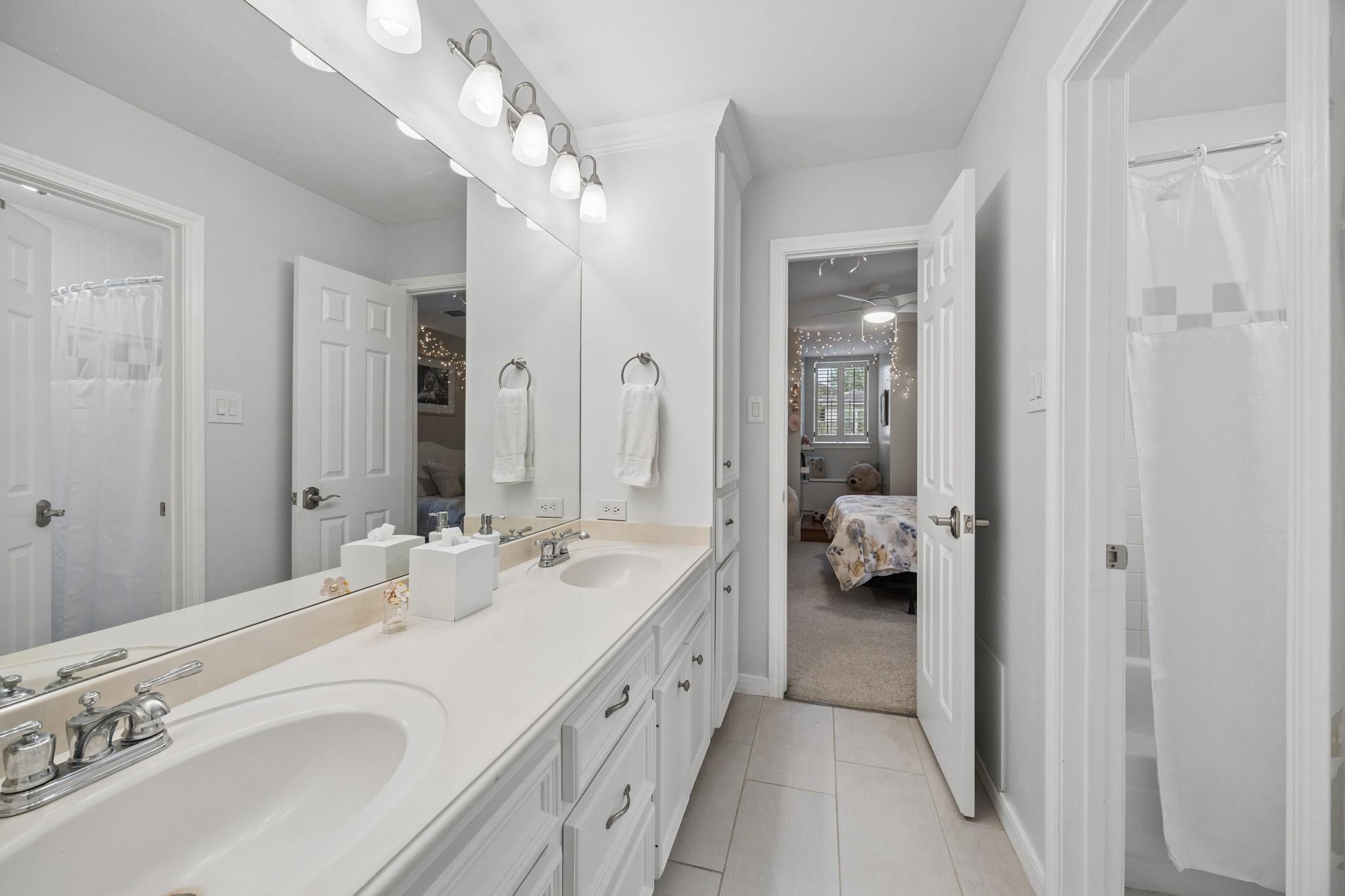 Bathroom with a long double-sink vanity and open doors to a bedroom.