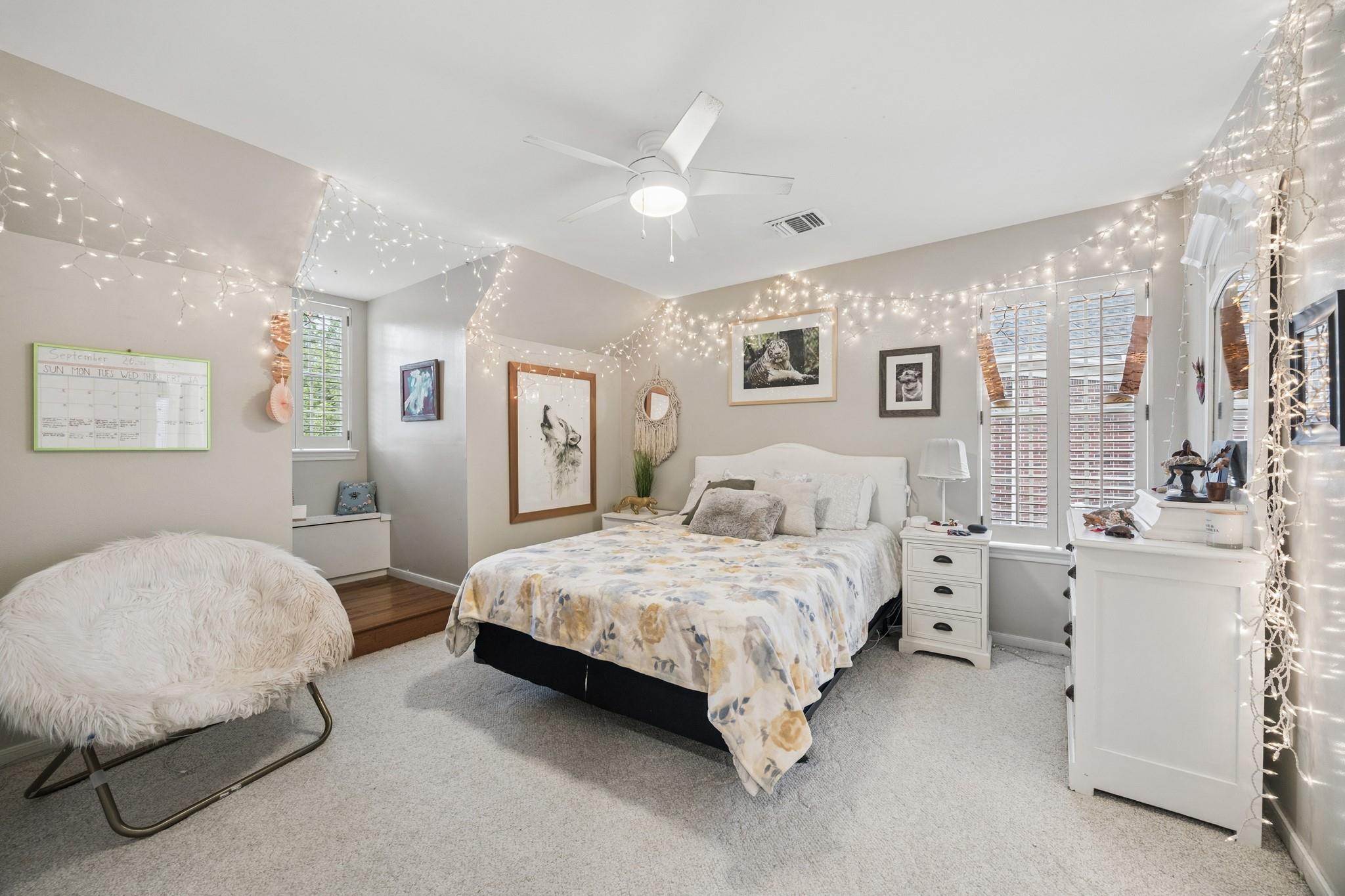 Bedroom with a pale floral bedspread, shuttered windows, and string lights along the walls.