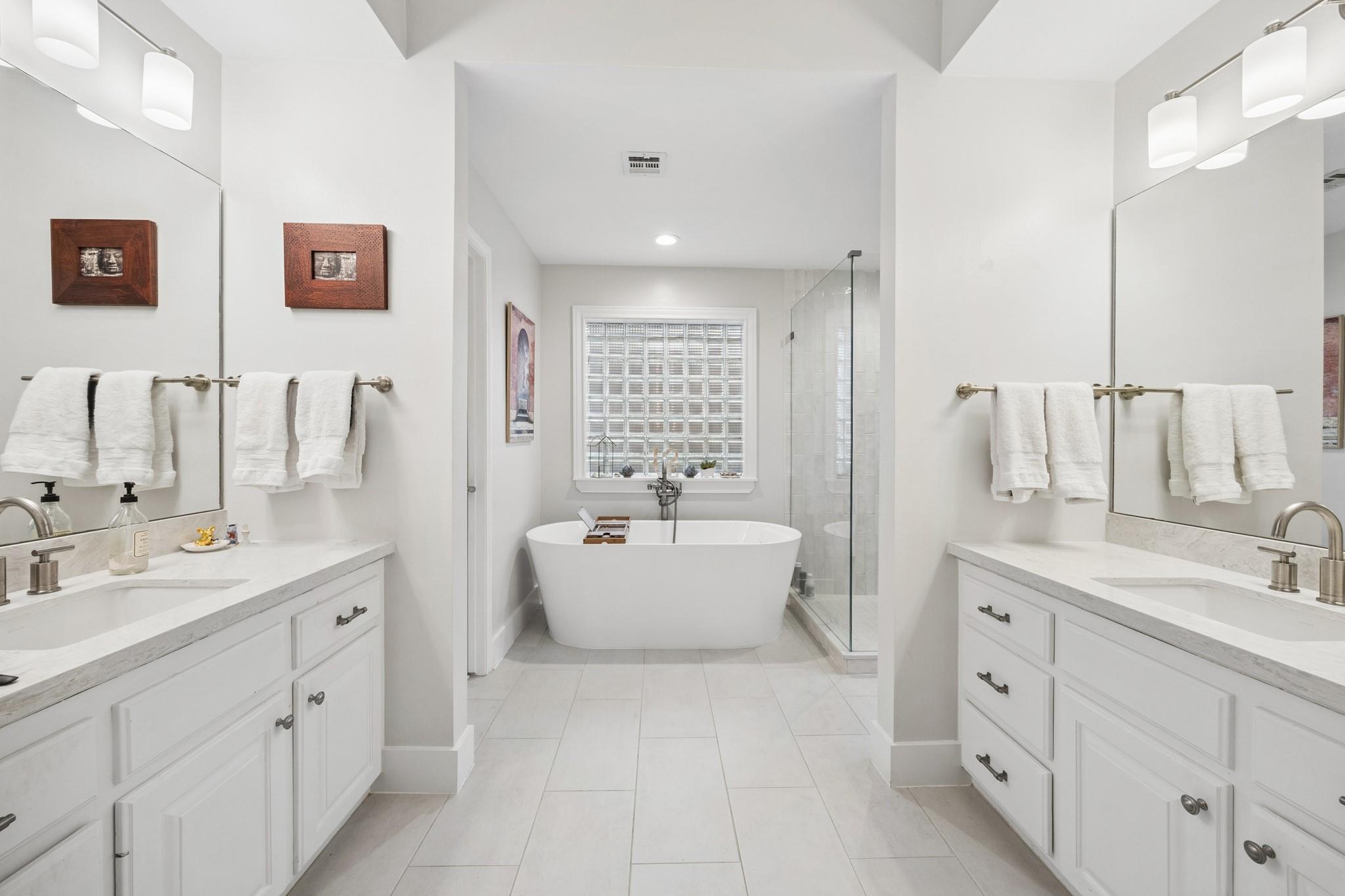 Primary bathroom with a freestanding tub, glass-block window, shower, and matching double vanities.