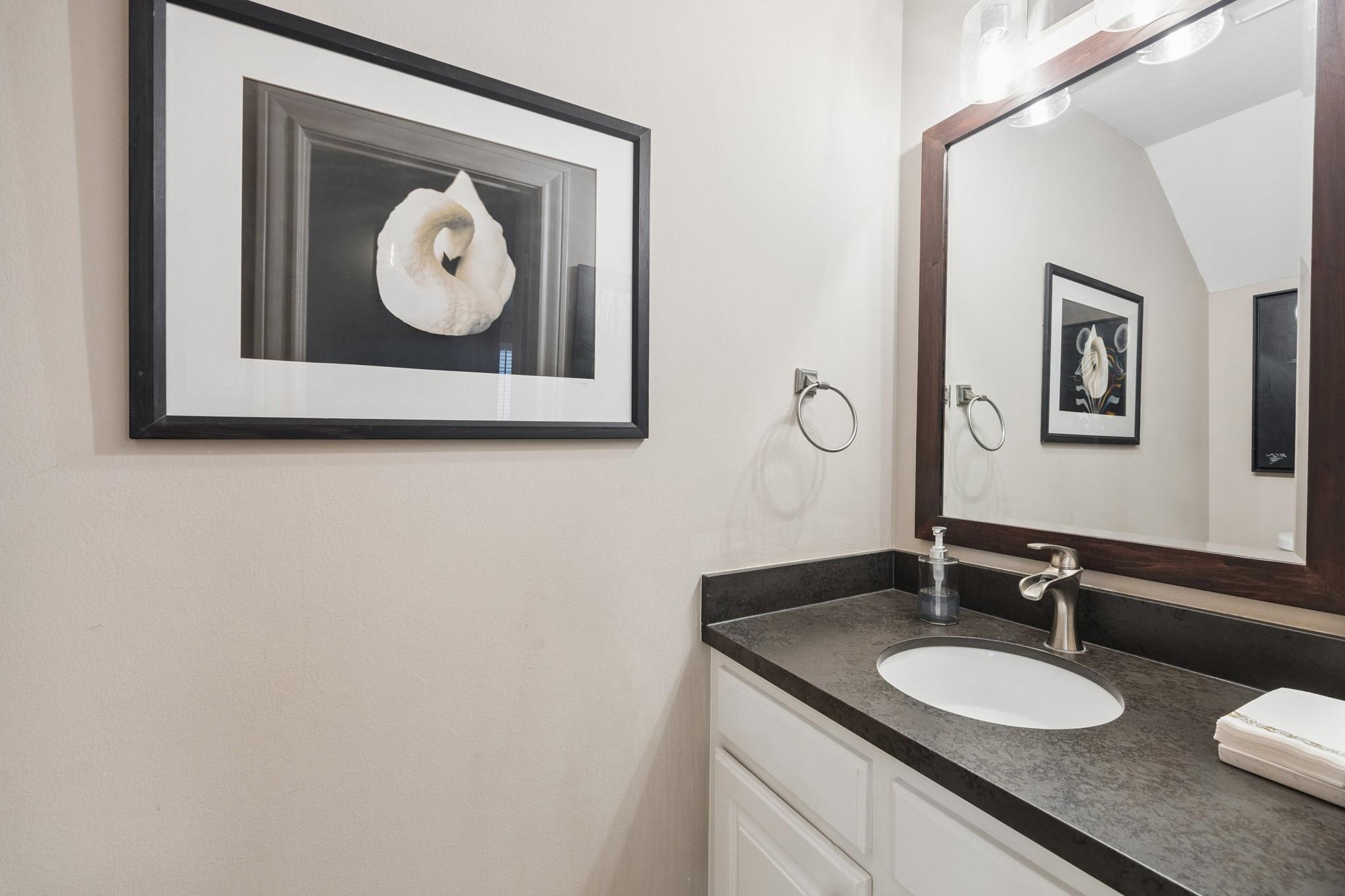 Bathroom vanity with a dark stone counter, oval sink, large wood-framed mirror, and framed wall art.