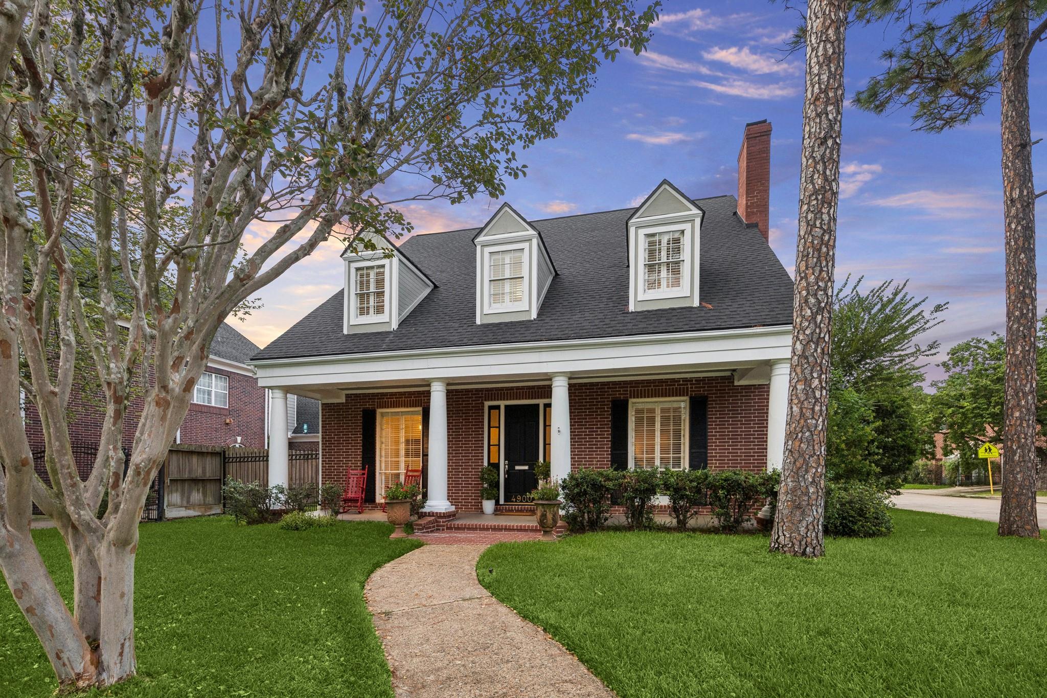 Red-brick house with white porch columns and three dormers, approached by a curved walkway through the lawn.