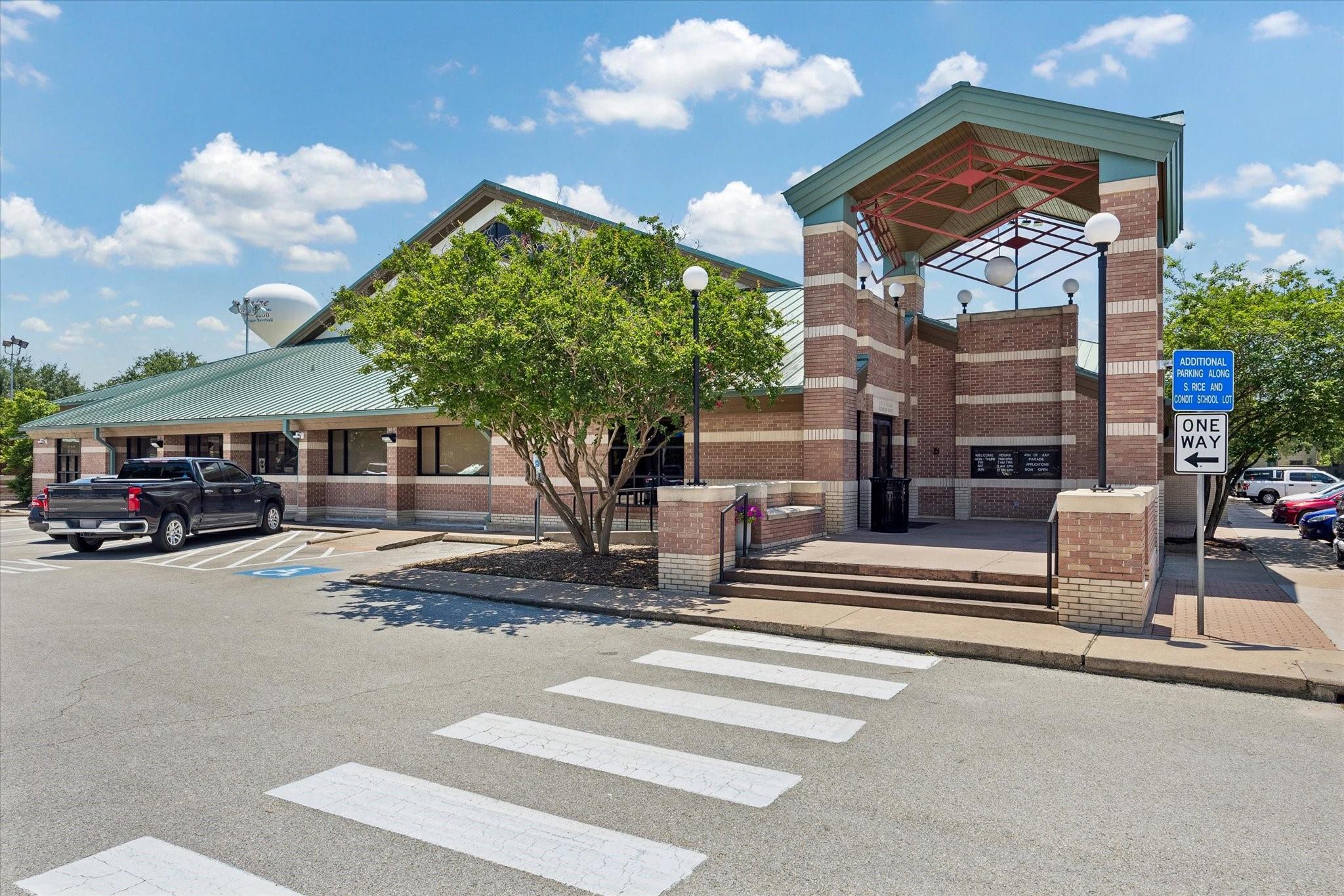 Brick school building with a green roof and covered entrance beside a marked crosswalk.