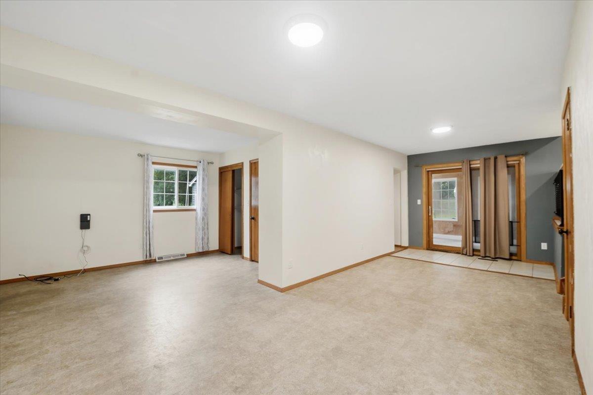 Empty open room with beige flooring, a window, and curtained glass doors.