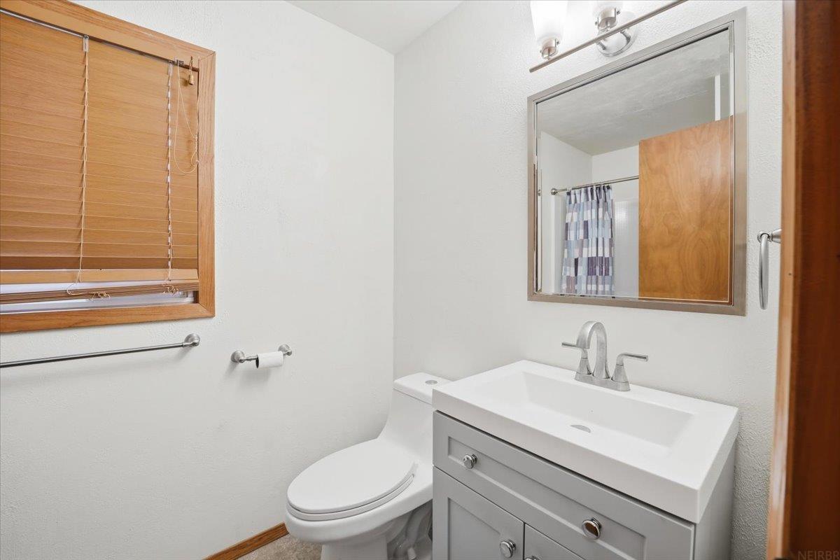 Bathroom with a gray vanity, white sink, toilet, and wood blinds.