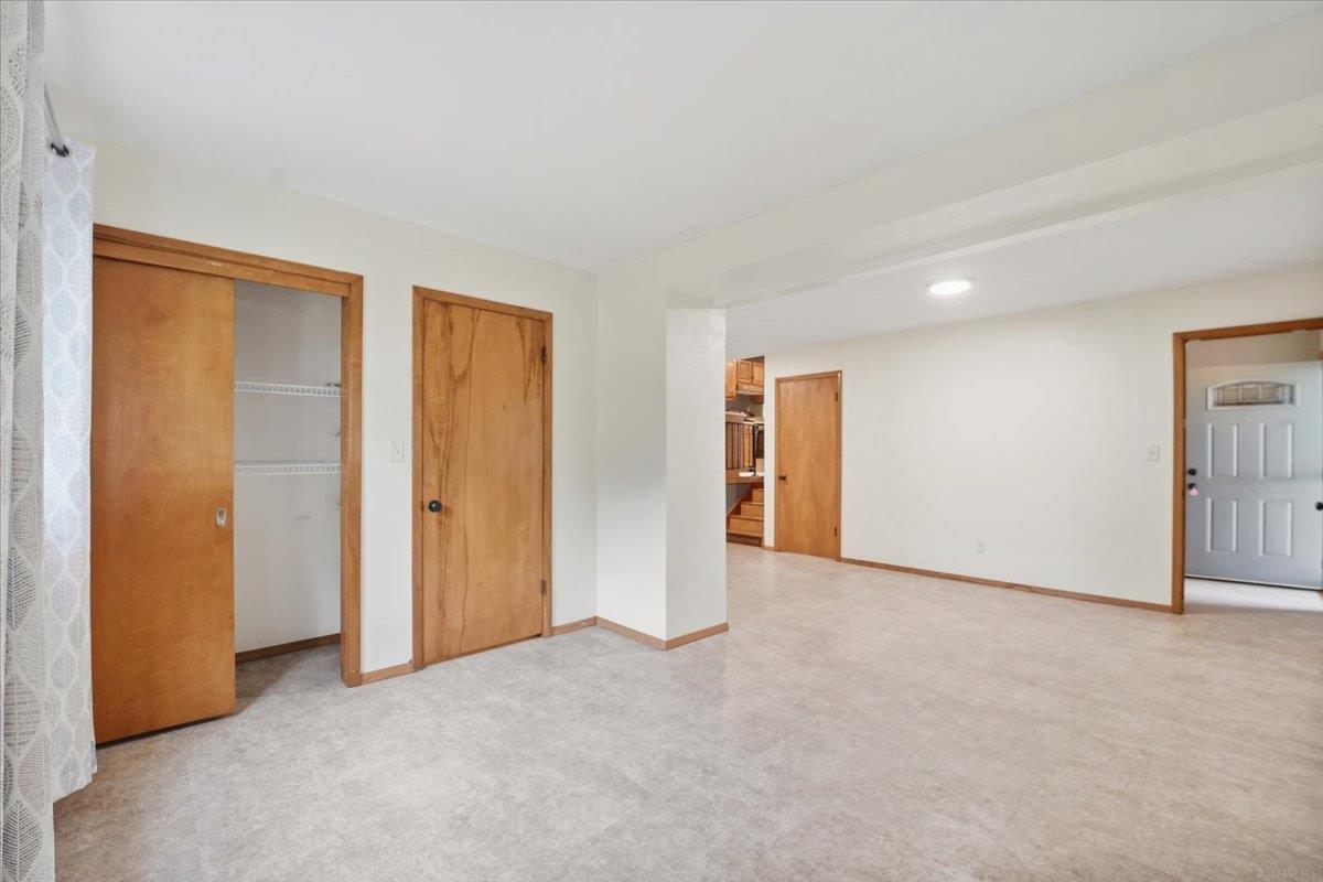 Vacant carpeted room with a sliding-door closet and wood-trimmed doorway toward the kitchen.