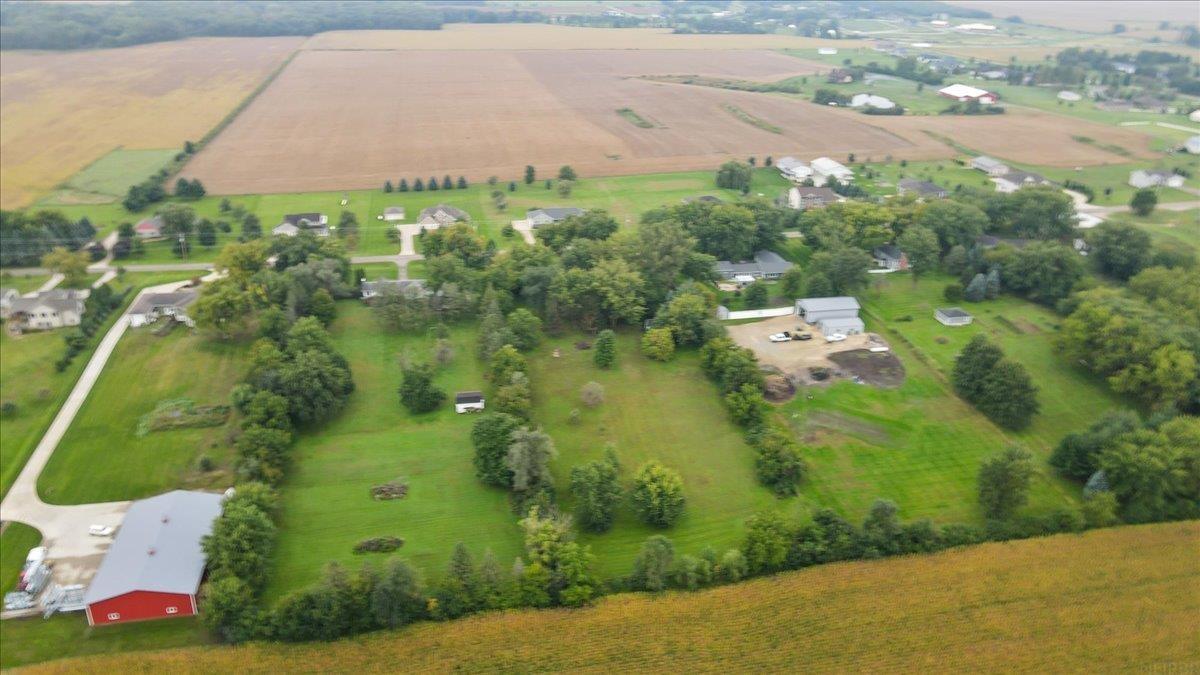 Aerial view of a rural property with a red barn, tree-dotted yard, and surrounding farmland.