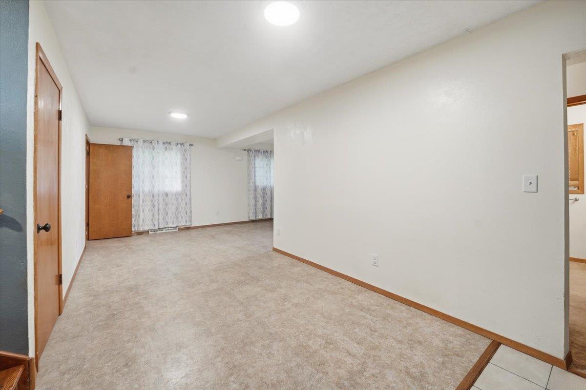 Vacant carpeted living room with curtained windows and wood trim.