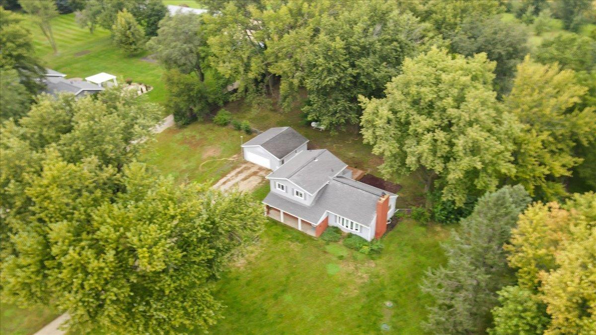 Aerial view of a house and detached garage amid mature trees and a broad lawn.