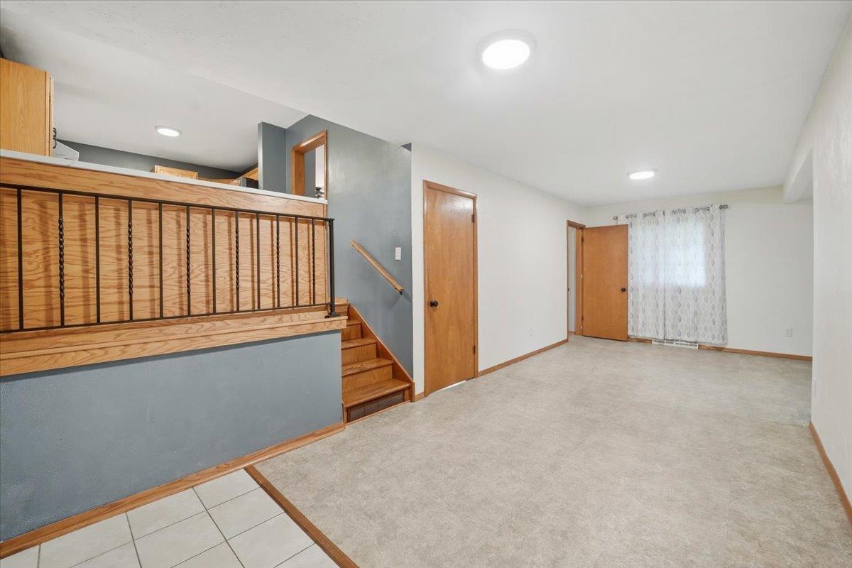 Empty carpeted living area with a wooden staircase and dark metal railing.
