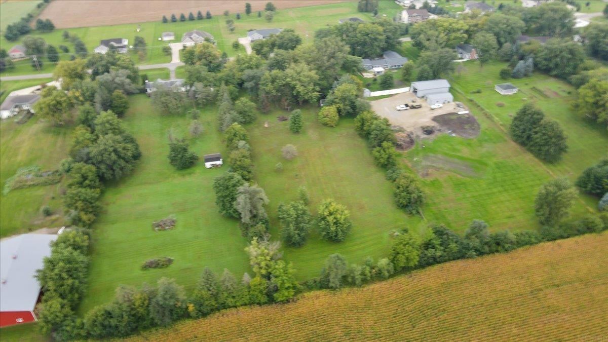 Aerial view of a rural property with open acreage, mature trees, and outbuildings.