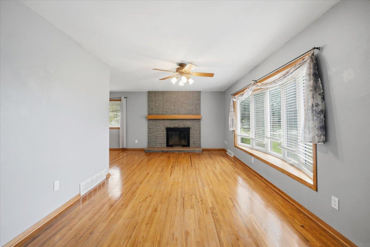 Empty living room with hardwood floors, a brick fireplace, and wide windows with blinds.