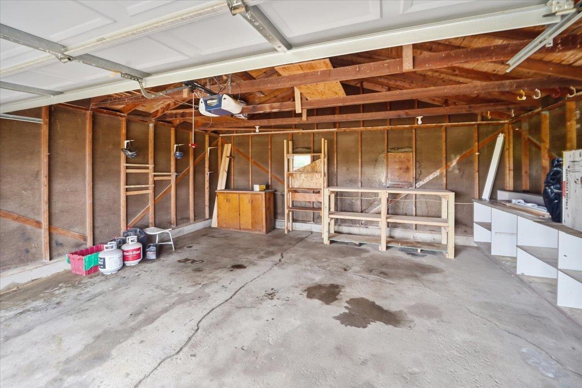 Unfinished garage with exposed wooden framing, concrete floor, and storage shelves.