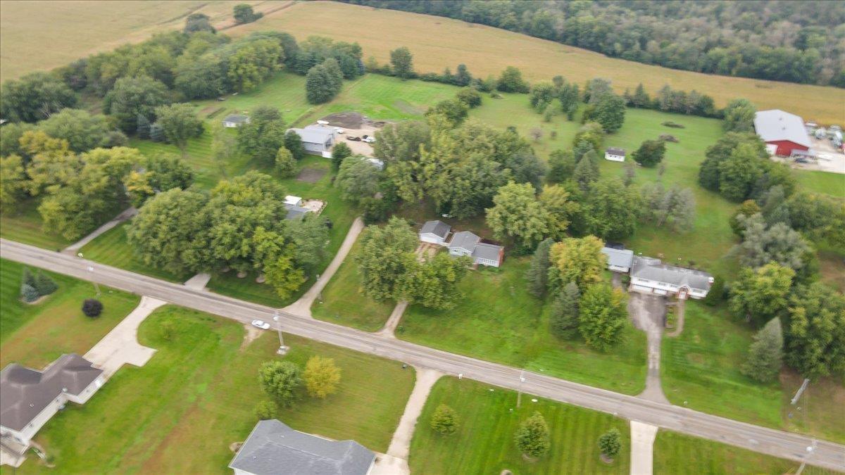 Aerial view of homes along a paved road, surrounded by trees and open fields.
