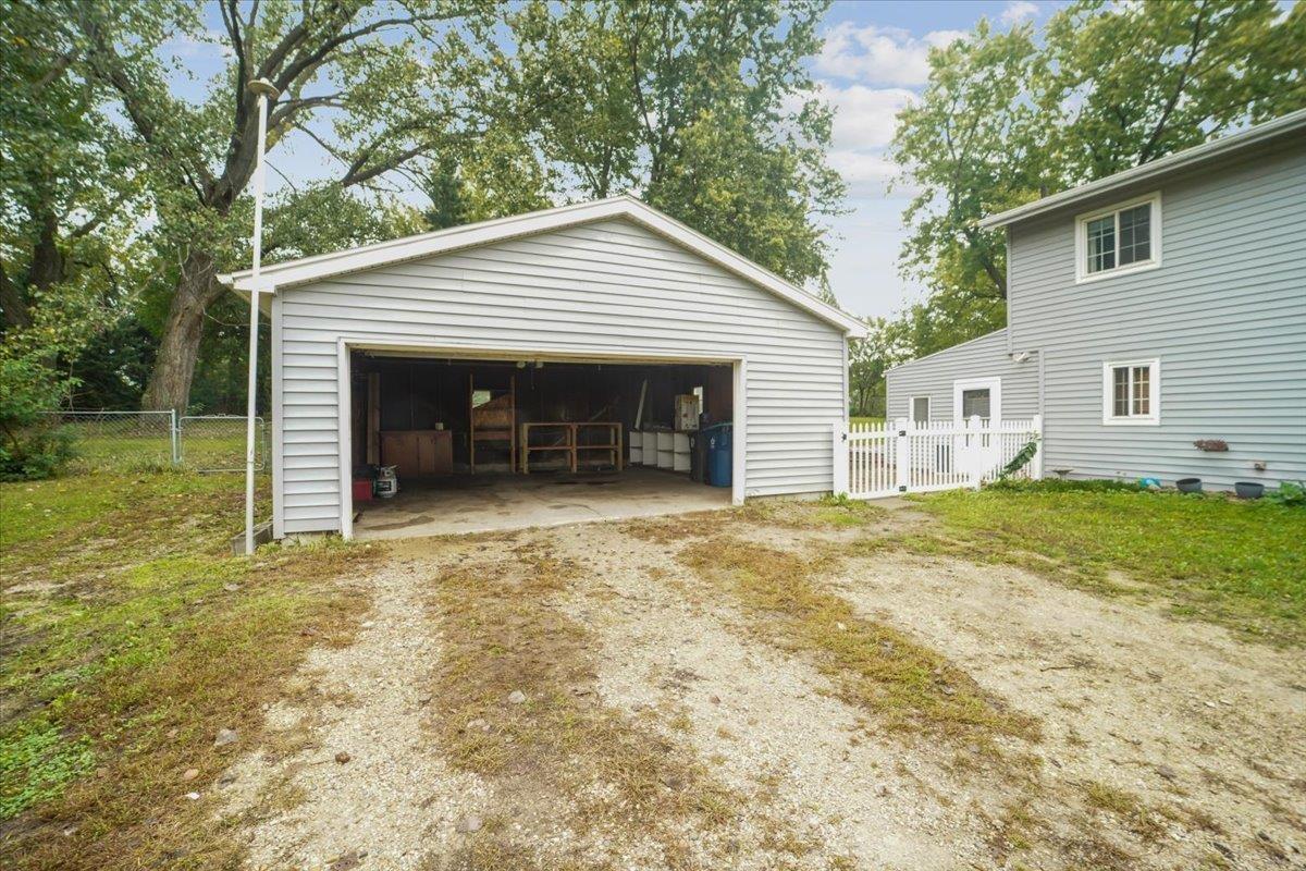 Detached garage with open door and workshop storage, beside a gray-sided house and gravel driveway.