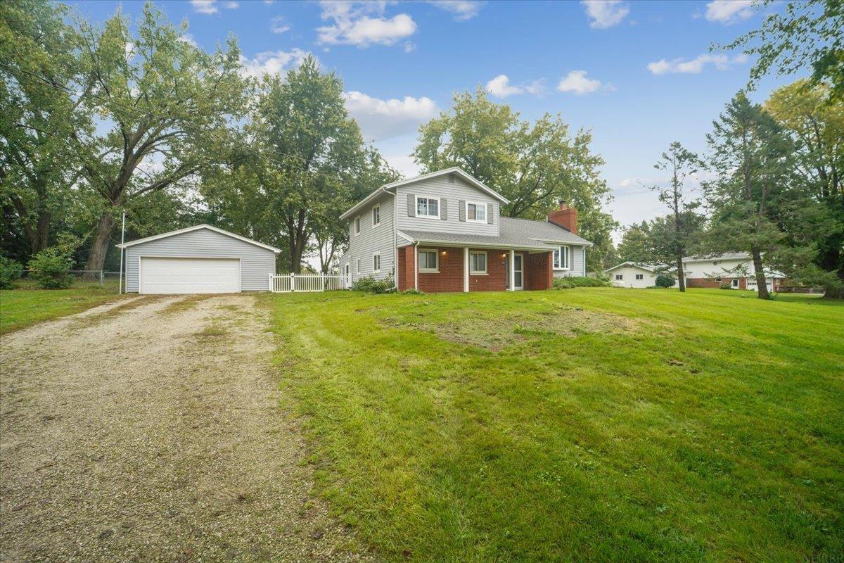 Two-story gray-sided home with a brick lower level, detached garage, and gravel driveway.