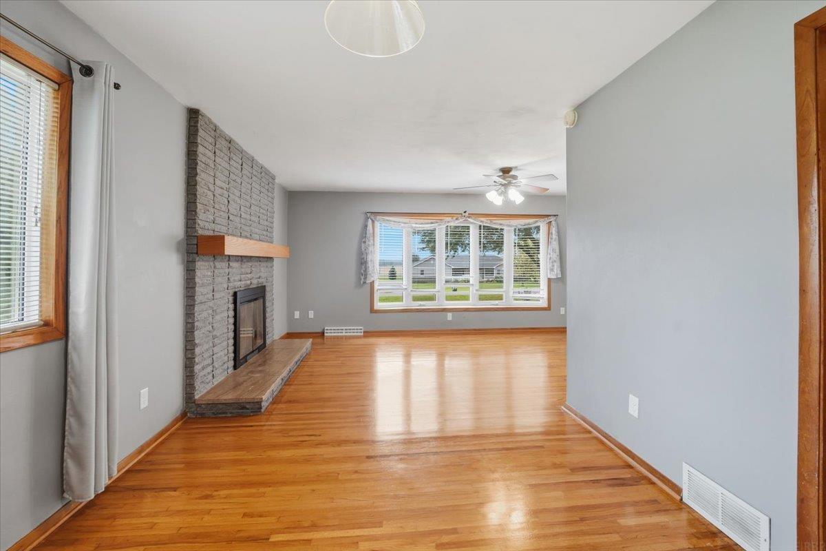 Empty living room with hardwood floors, gray brick fireplace, and a wide window.