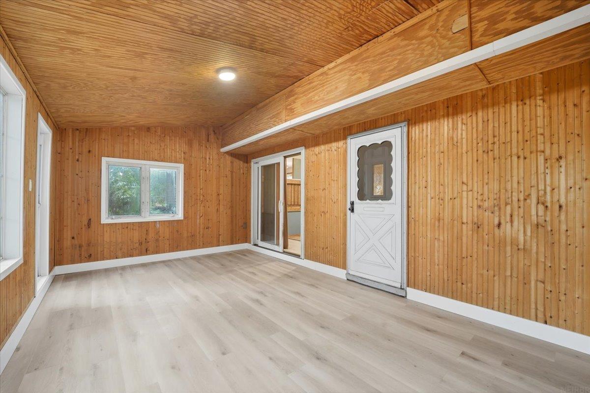 Empty wood-paneled room with pale flooring, several windows, and a white exterior door.