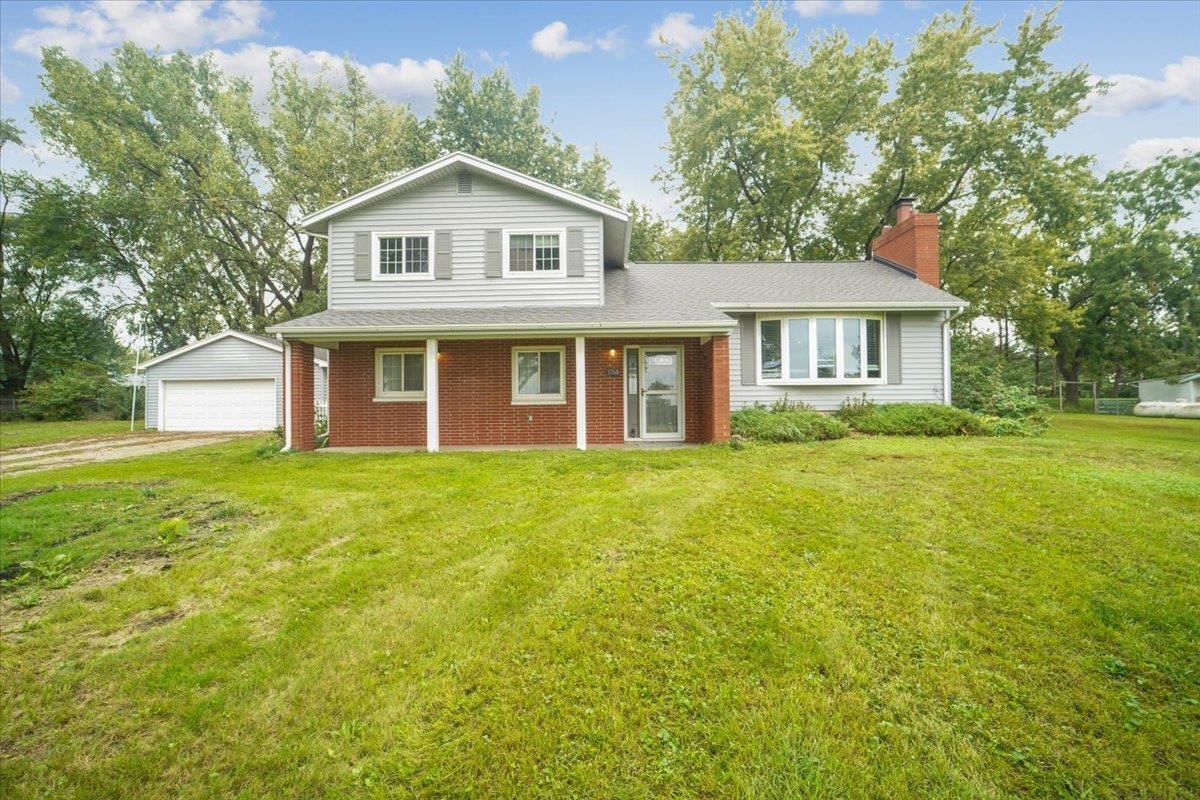 Split-level home with gray siding, red brick facade, attached garage, and a broad front lawn.