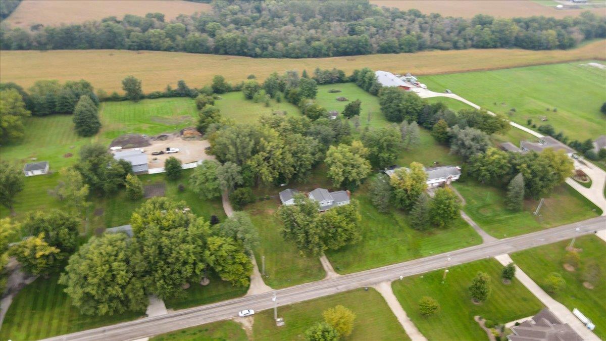 Aerial view of a tree-filled rural property with homes, outbuildings, open fields, and a road frontage.