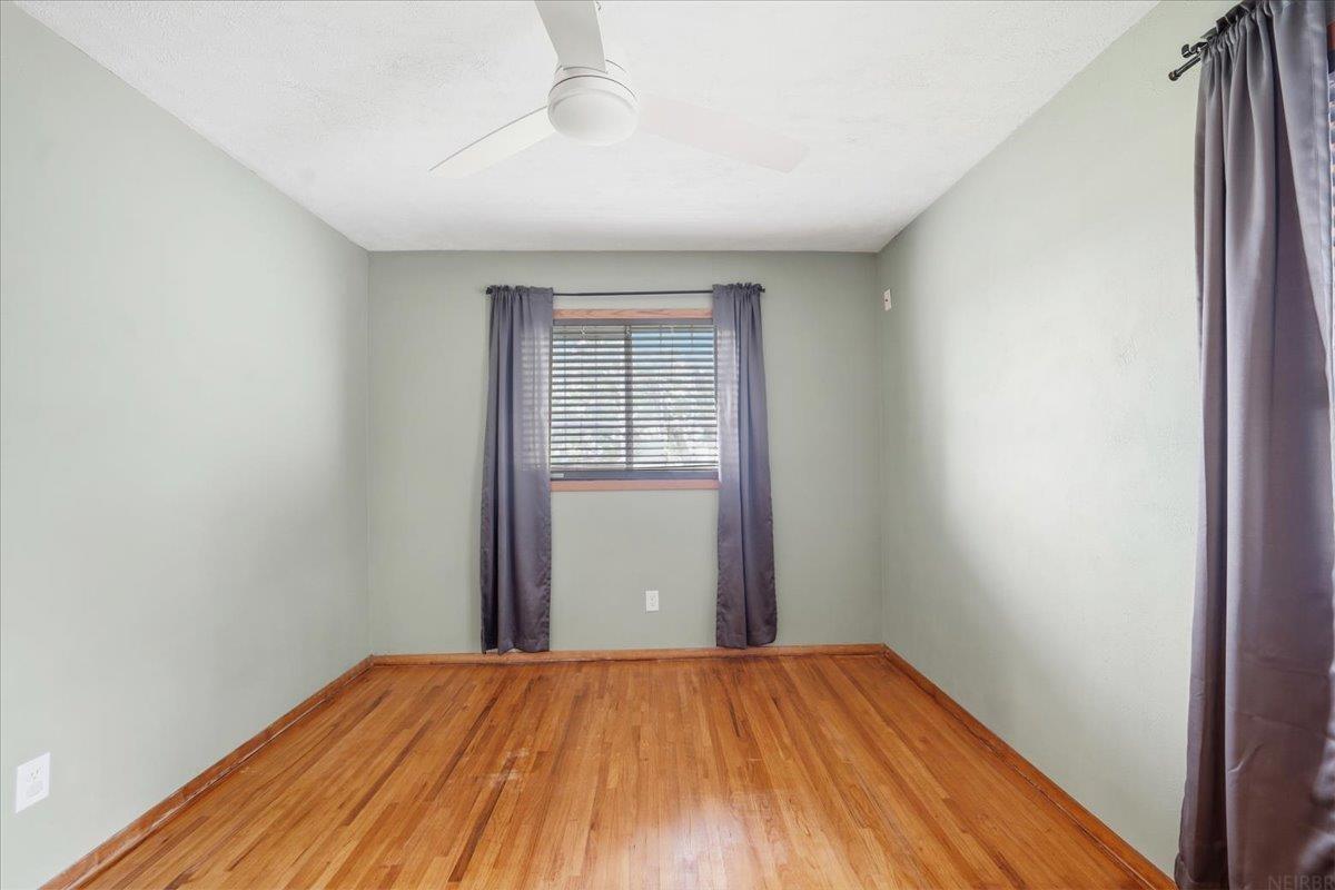 Empty bedroom with hardwood floors, purple curtains, and a ceiling fan.